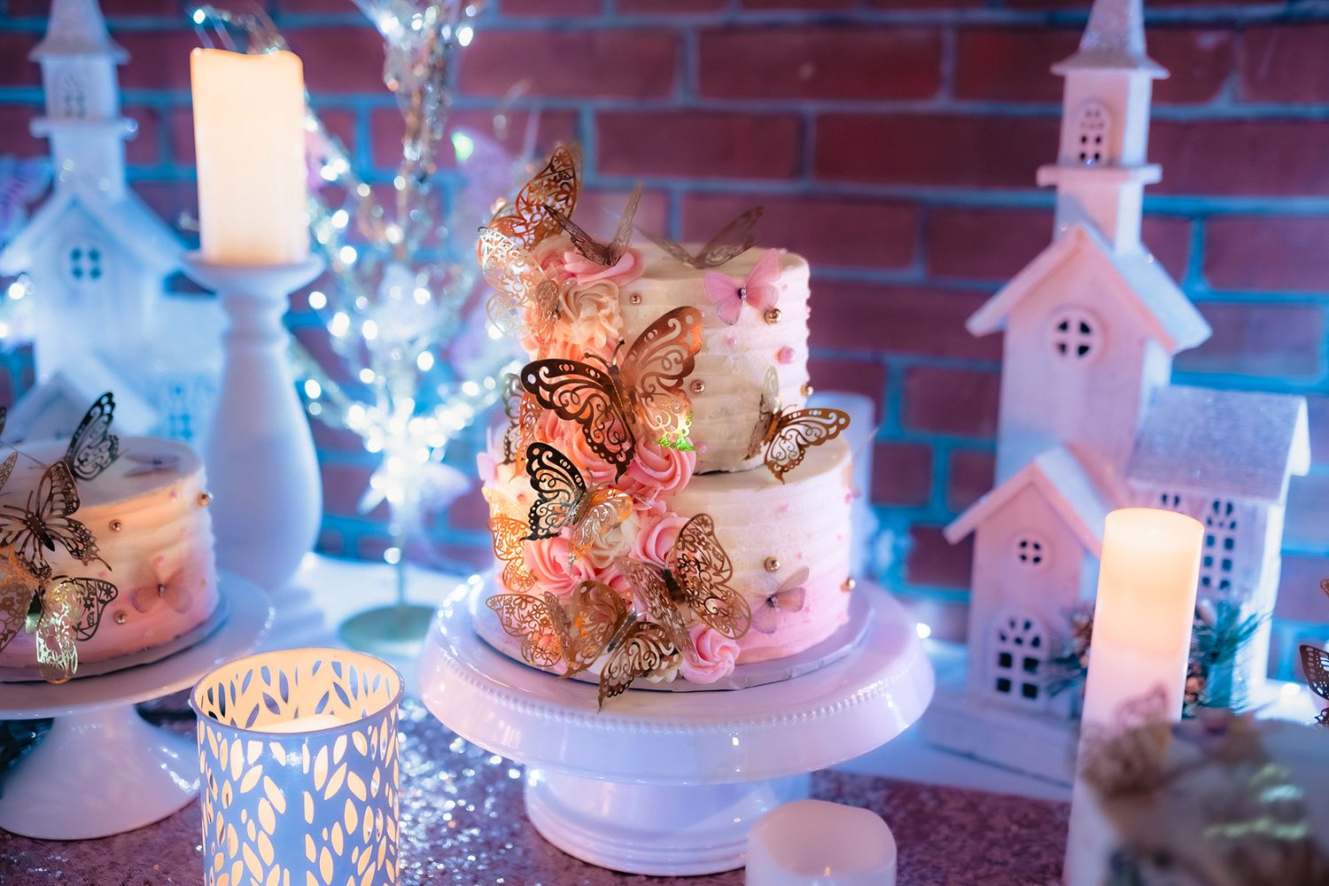 Elegant white wedding cake display with soft lighting and brick wall backdrop featuring delicate decorative details.