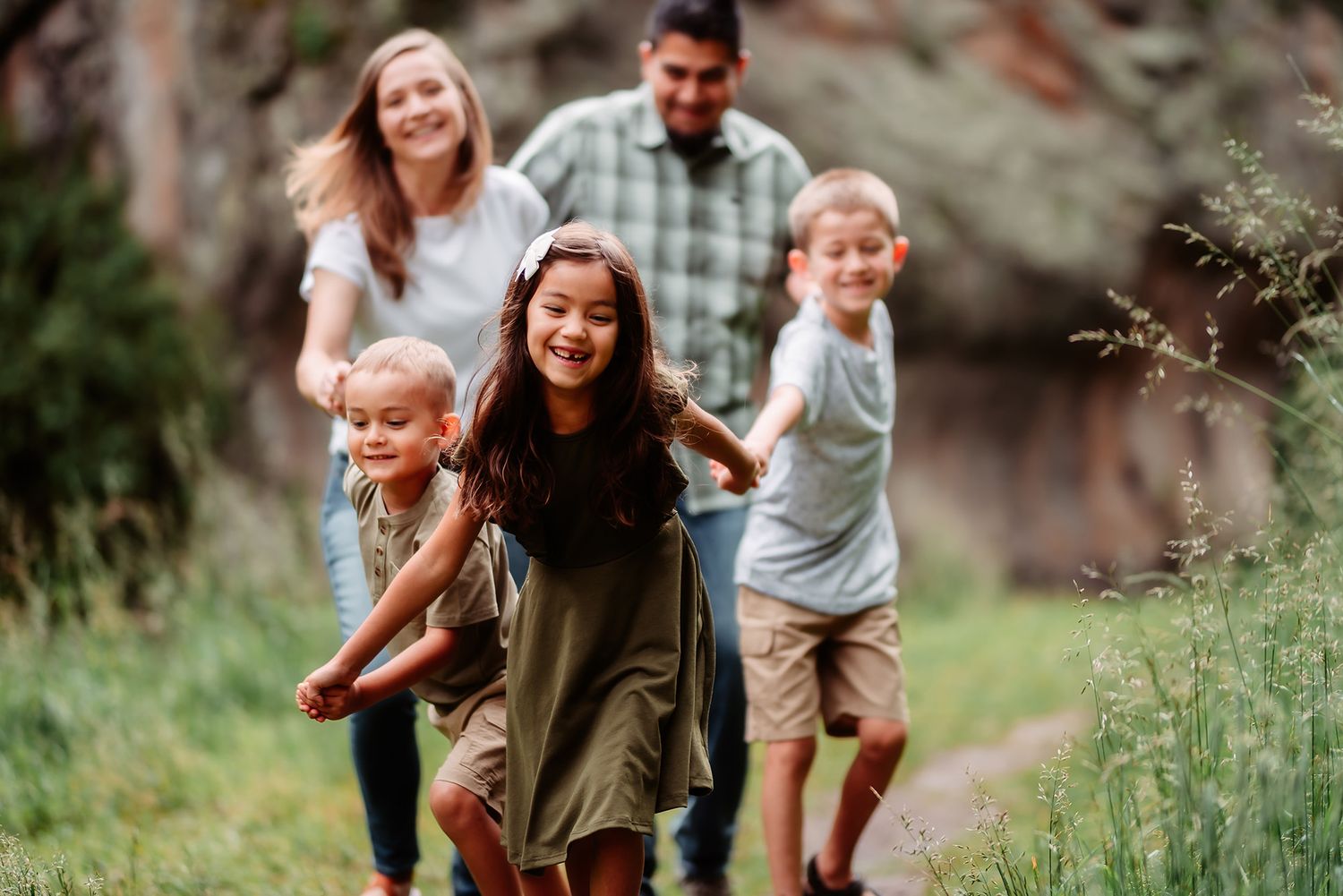 Family enjoys playful moments together while walking through a lush green outdoor path during golden hour.