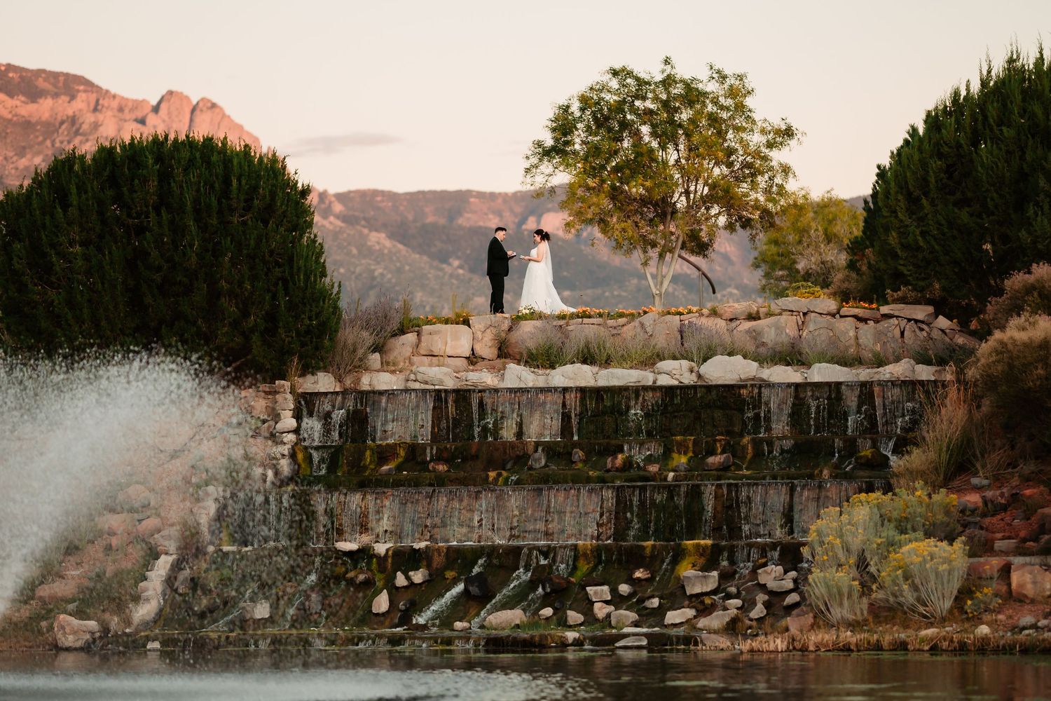 A panoramic view of a stone wall and trees against a mountain landscape during sunset.
