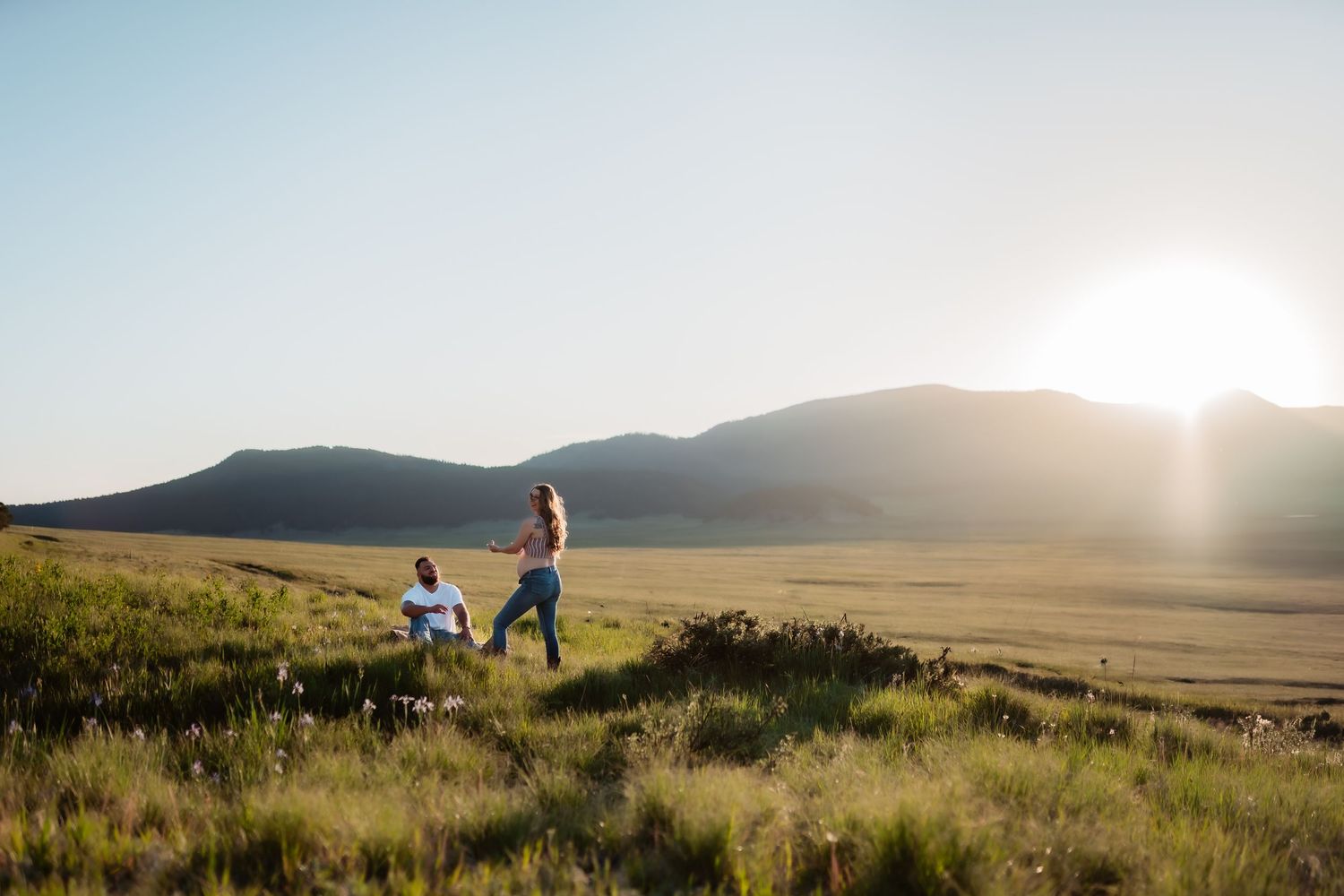 A scenic view of rolling hills and grasslands at sunset with people walking in the distance.