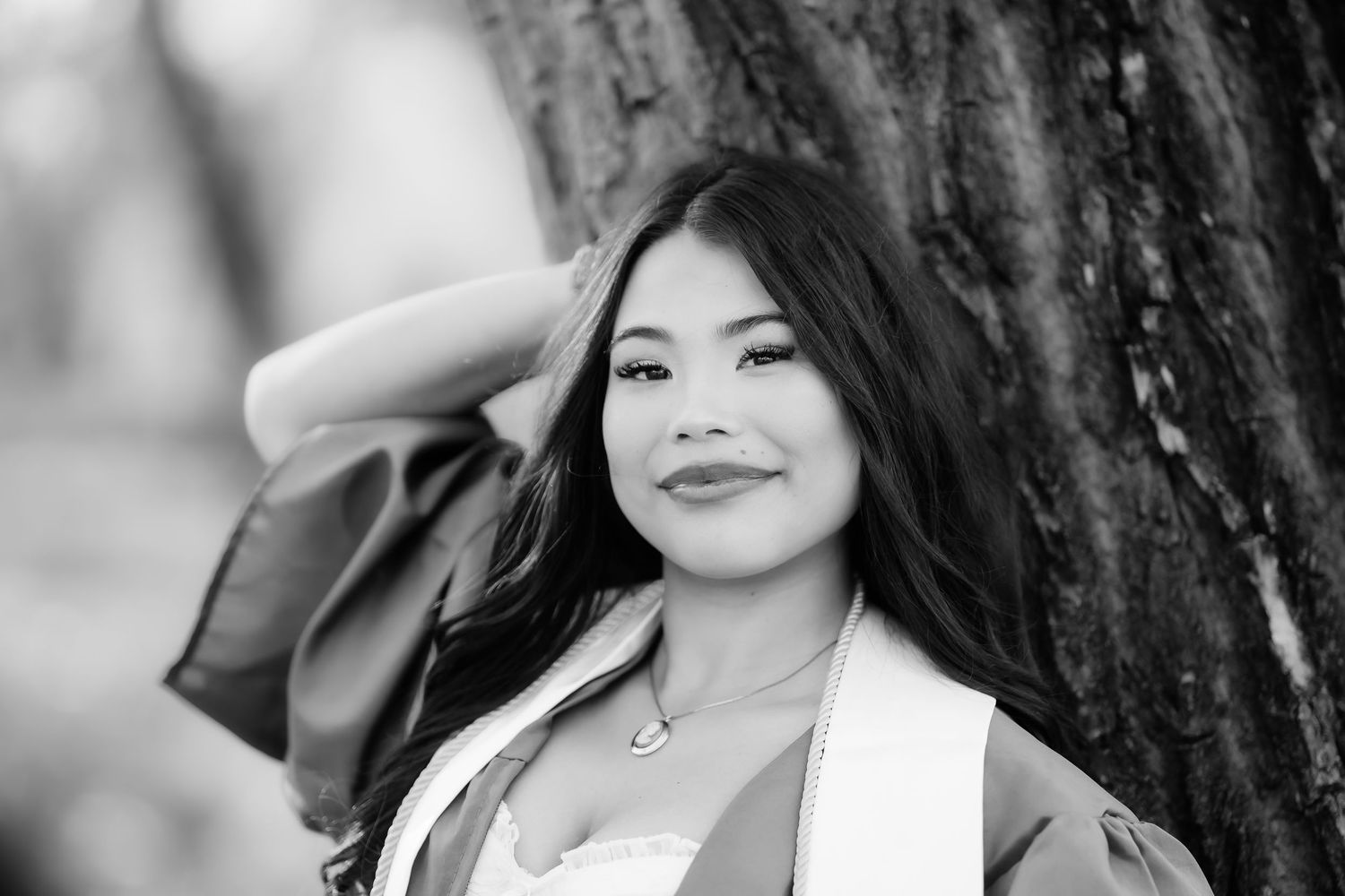 Black and white headshot with person wearing white jacket against tree background.