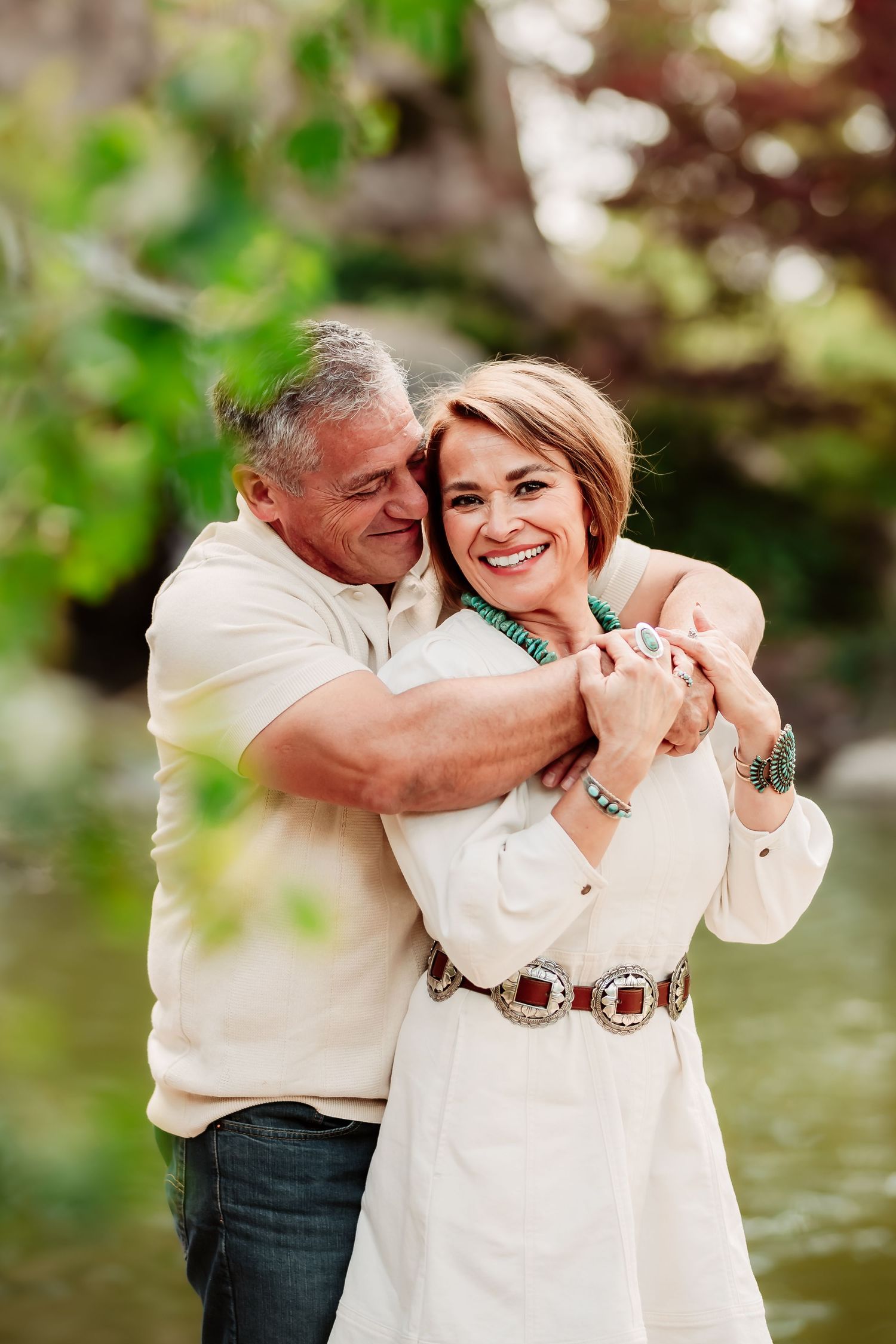A couple embraces and laughs together during an outdoor photoshoot near water.