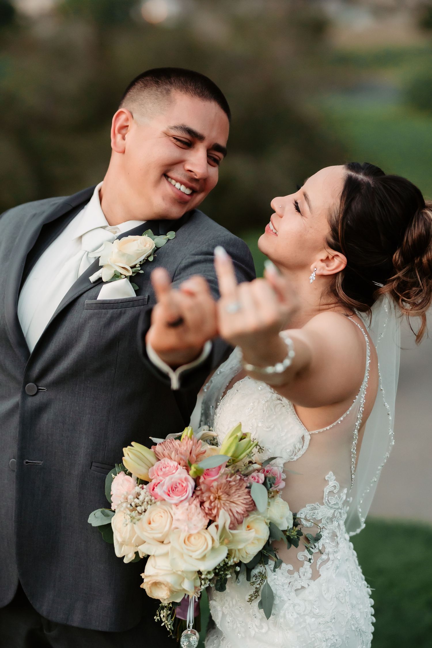 Joyful couple laughs together while holding a bridal bouquet of pink and cream roses.