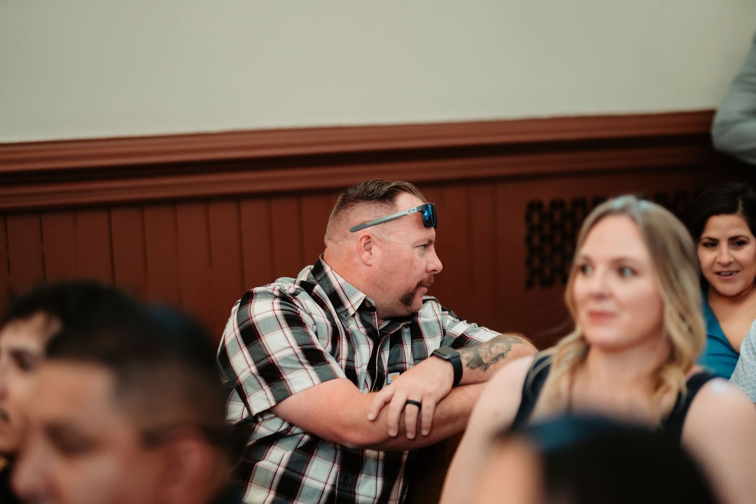 A person in a plaid shirt laughs while seated in a crowd at an event.