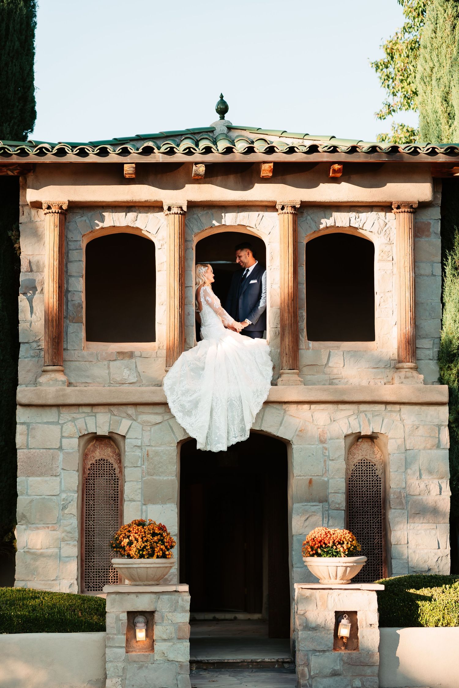 A stone archway with columns and terracotta roof tiles creates an elegant covered walkway in a Mediterranean style garden.
