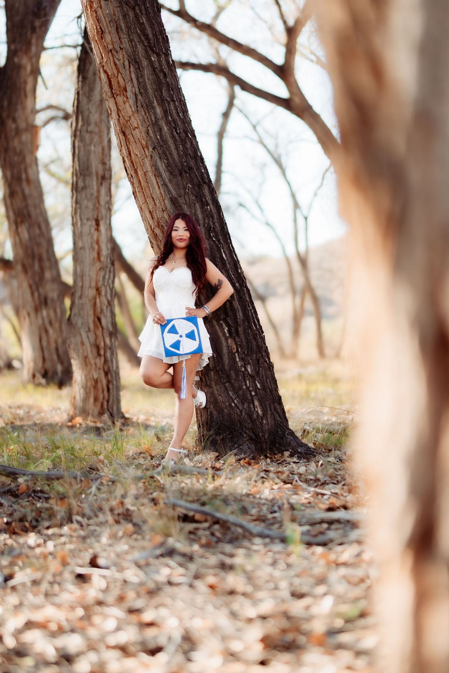 Artistic outdoor portrait with person leaning against tree trunk holding blue circular sign.