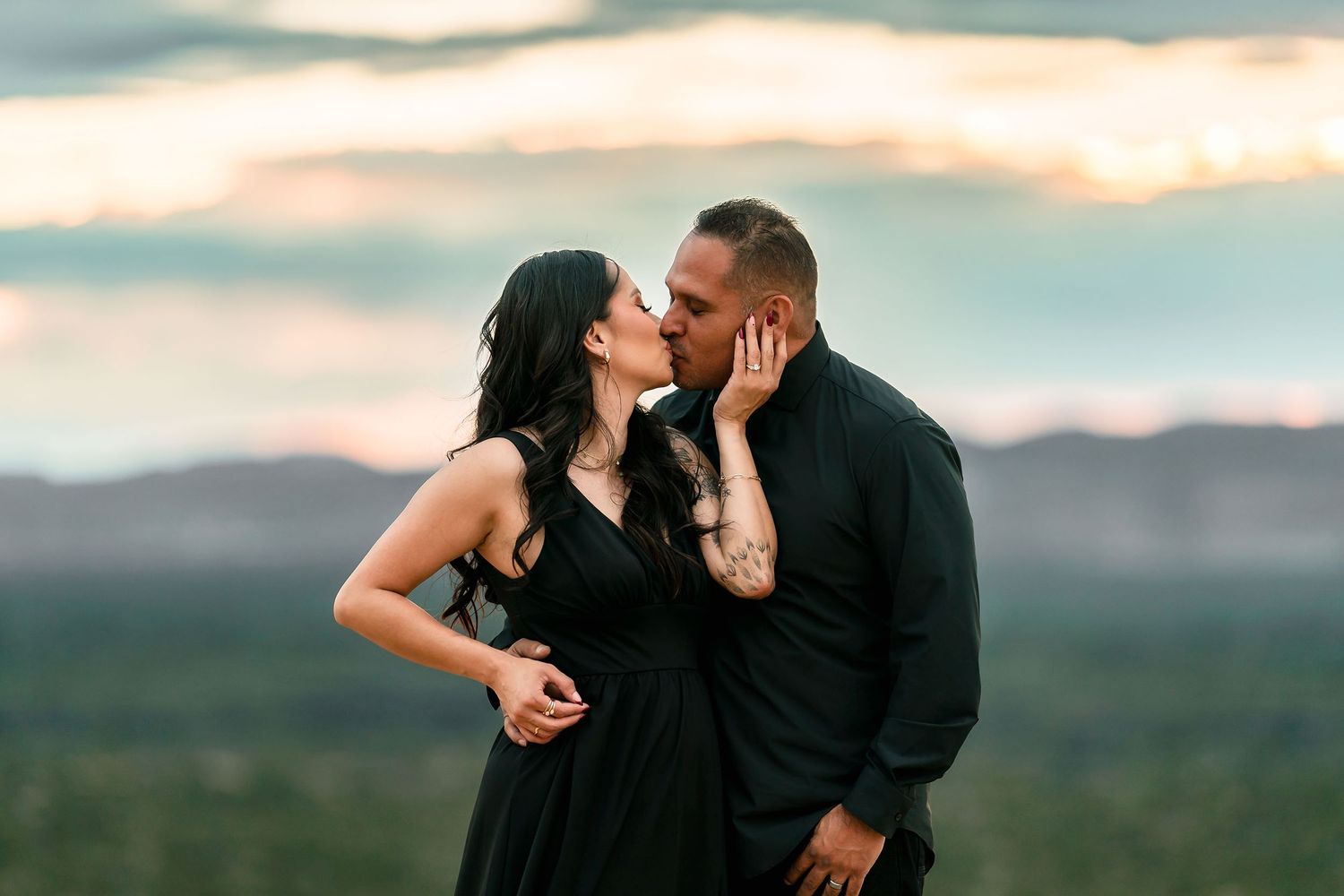 Couple sharing a romantic kiss at golden hour with scenic mountain backdrop.