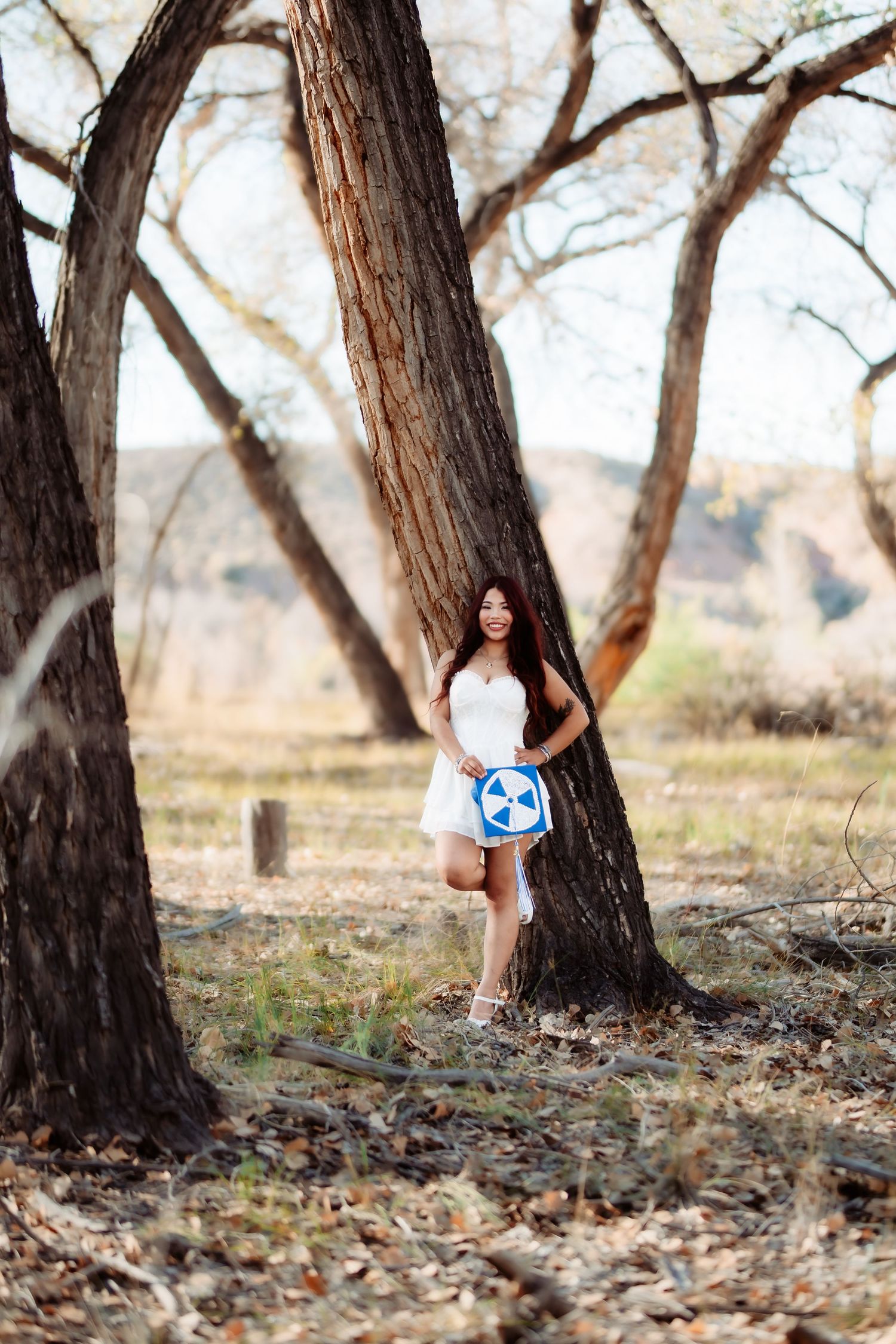 Scenic woodland photo with person in white dress posing against tree with mountains in background.