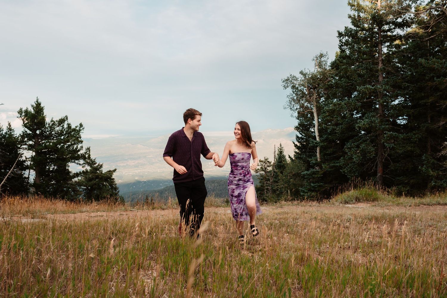 Couple runs and plays together through mountain meadow with scenic mountain backdrop.