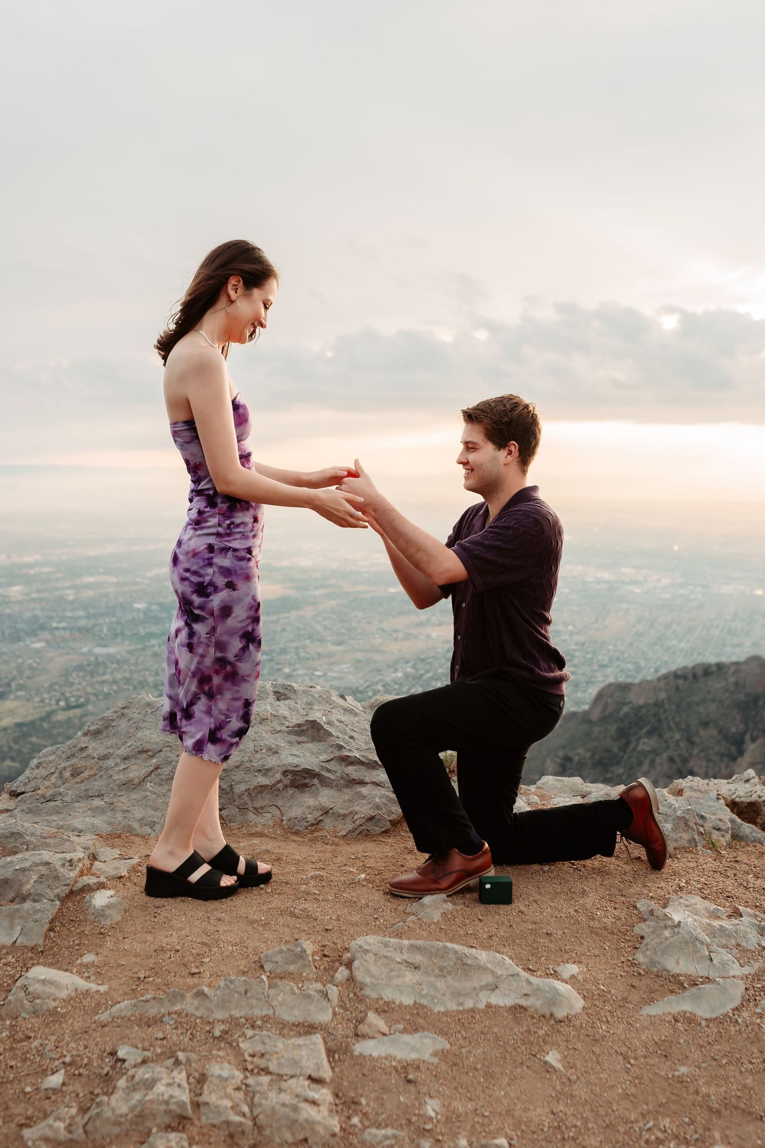 A romantic marriage proposal taking place on a mountain overlook at sunset.