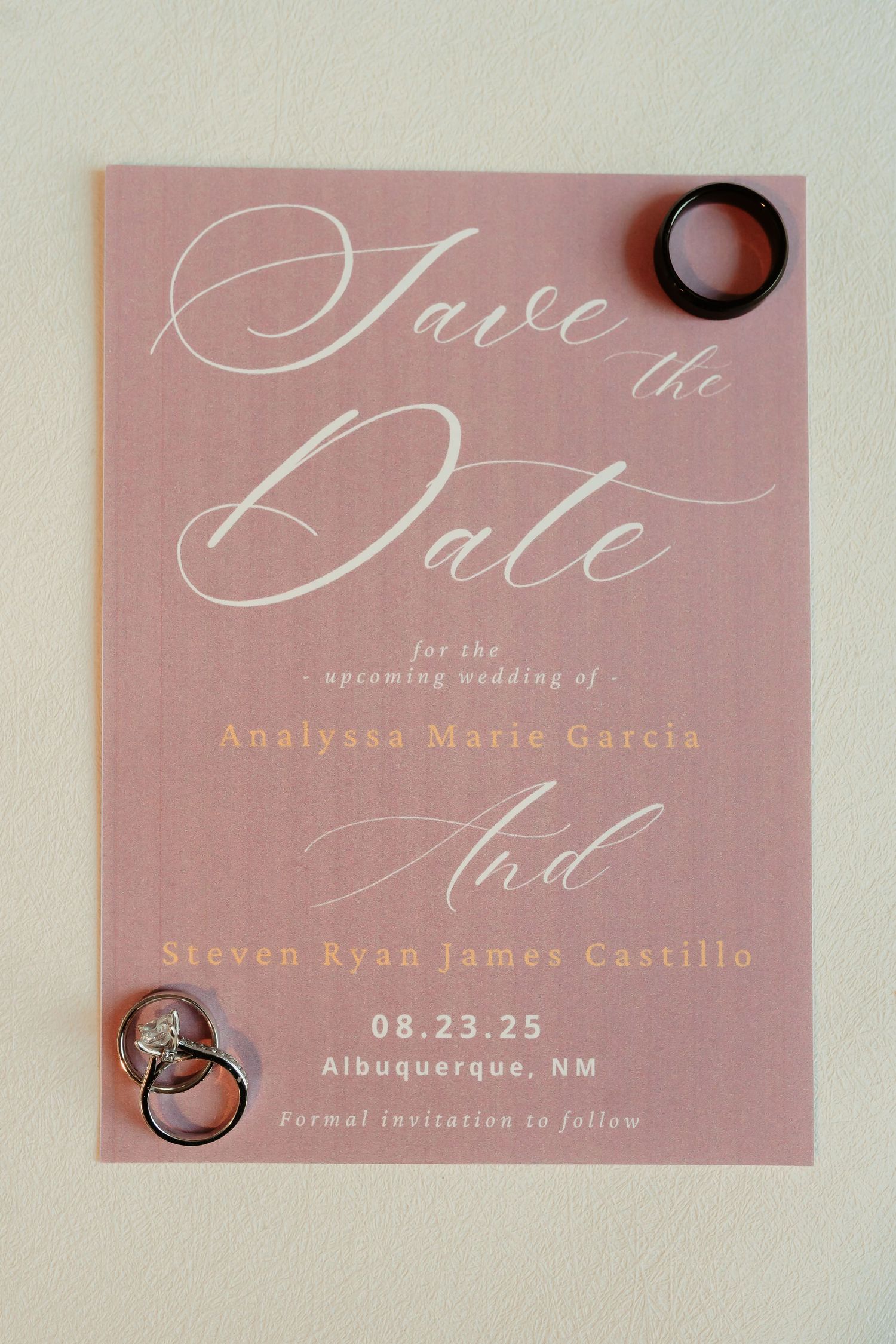 Blush pink wedding save the date cards with elegant calligraphy text and ring details in soft lighting.