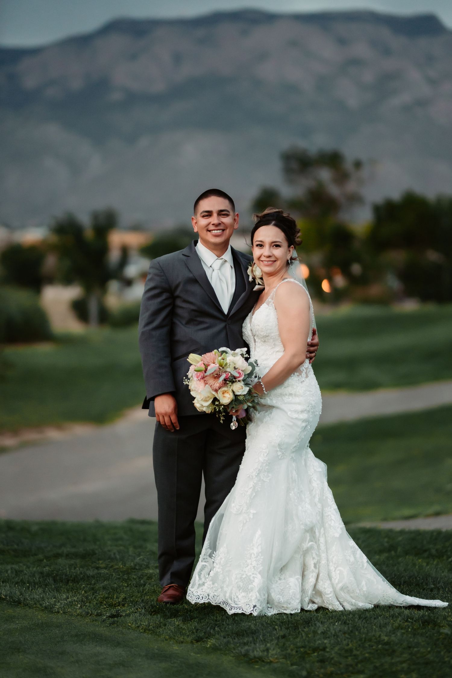 Wedding couple posing on golf course with dramatic mountain landscape backdrop.