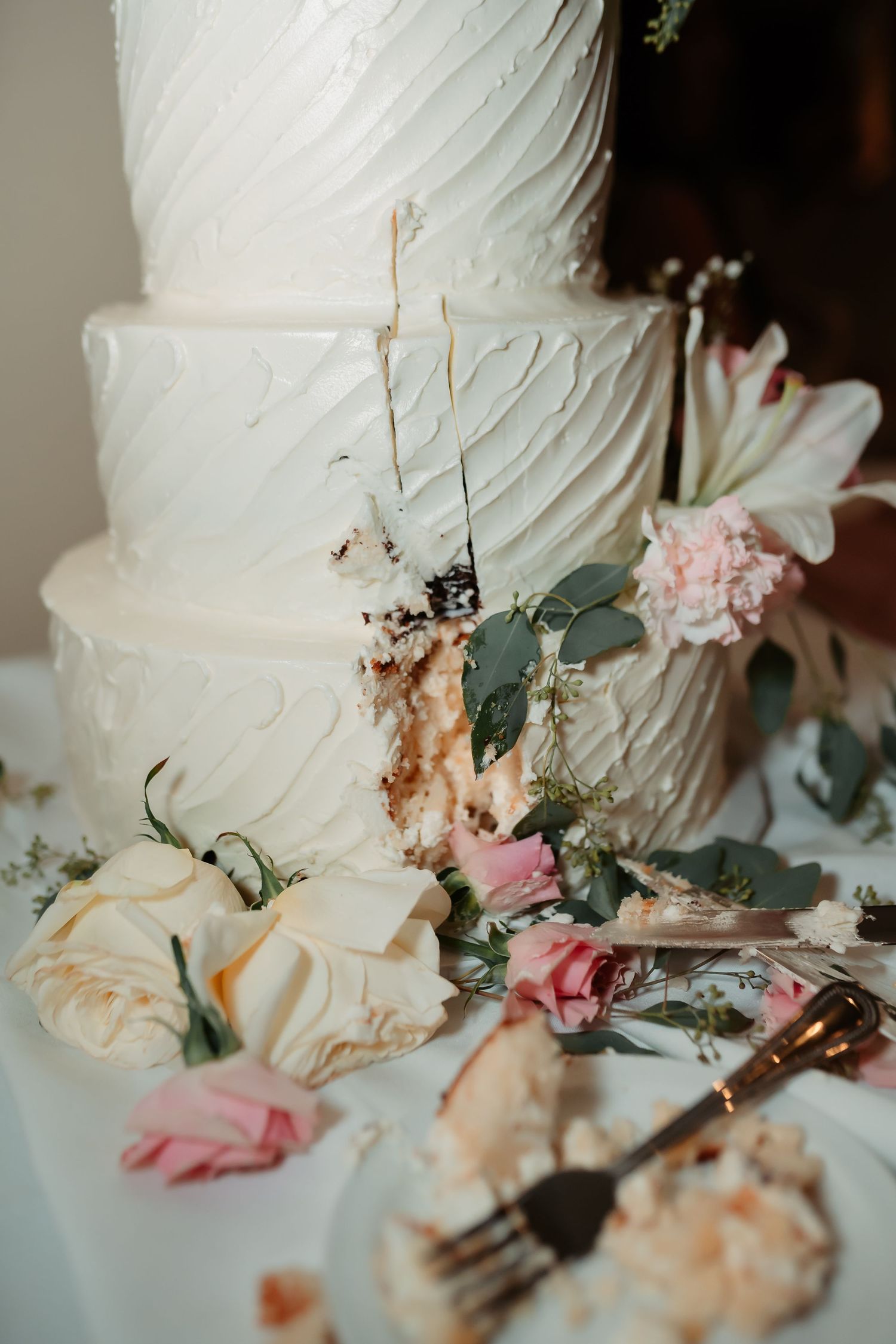 Elegant white wedding cake decorated with pink roses and eucalyptus leaves.