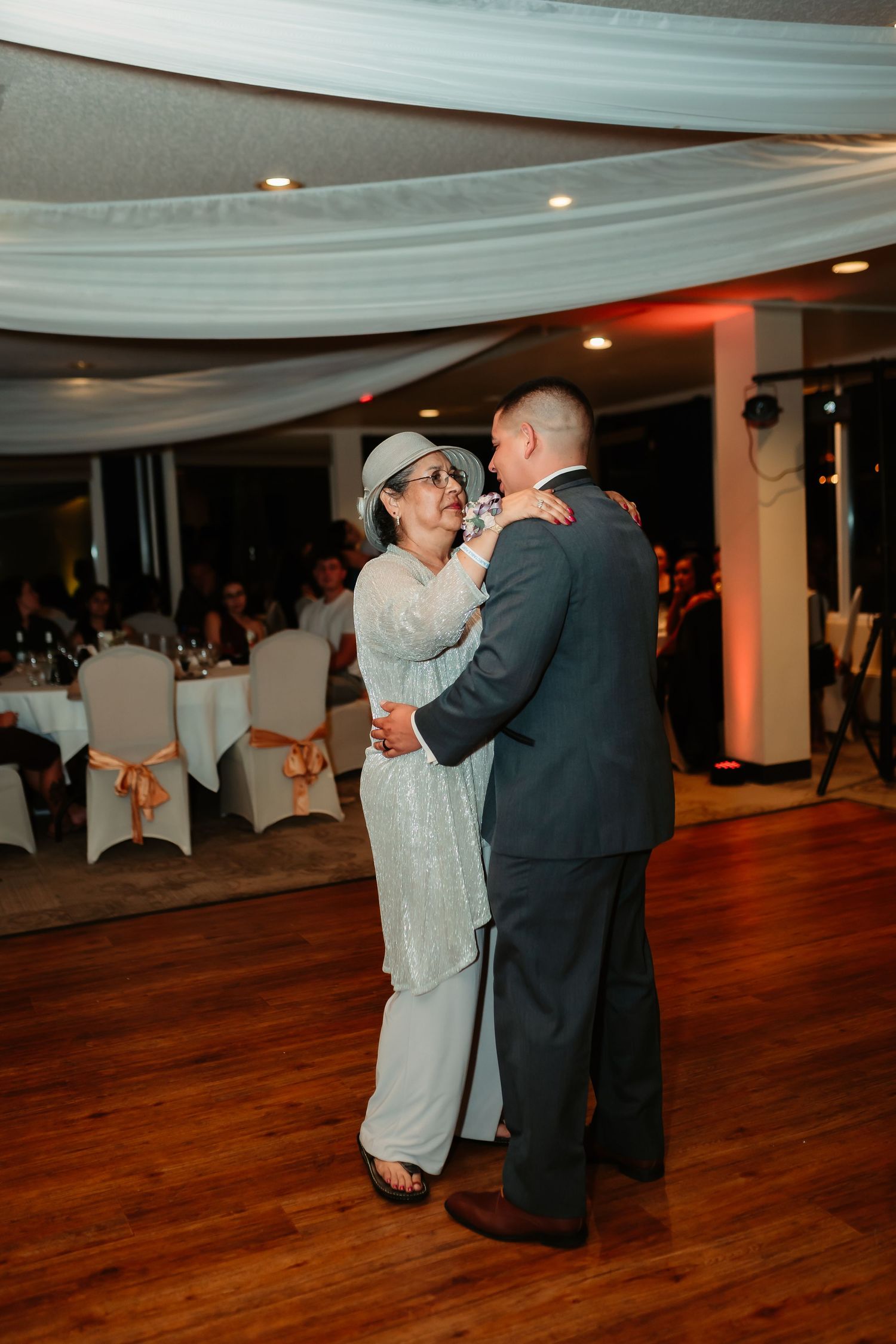 A wedding reception dance scene shows couples swaying under draped white ceiling decorations.