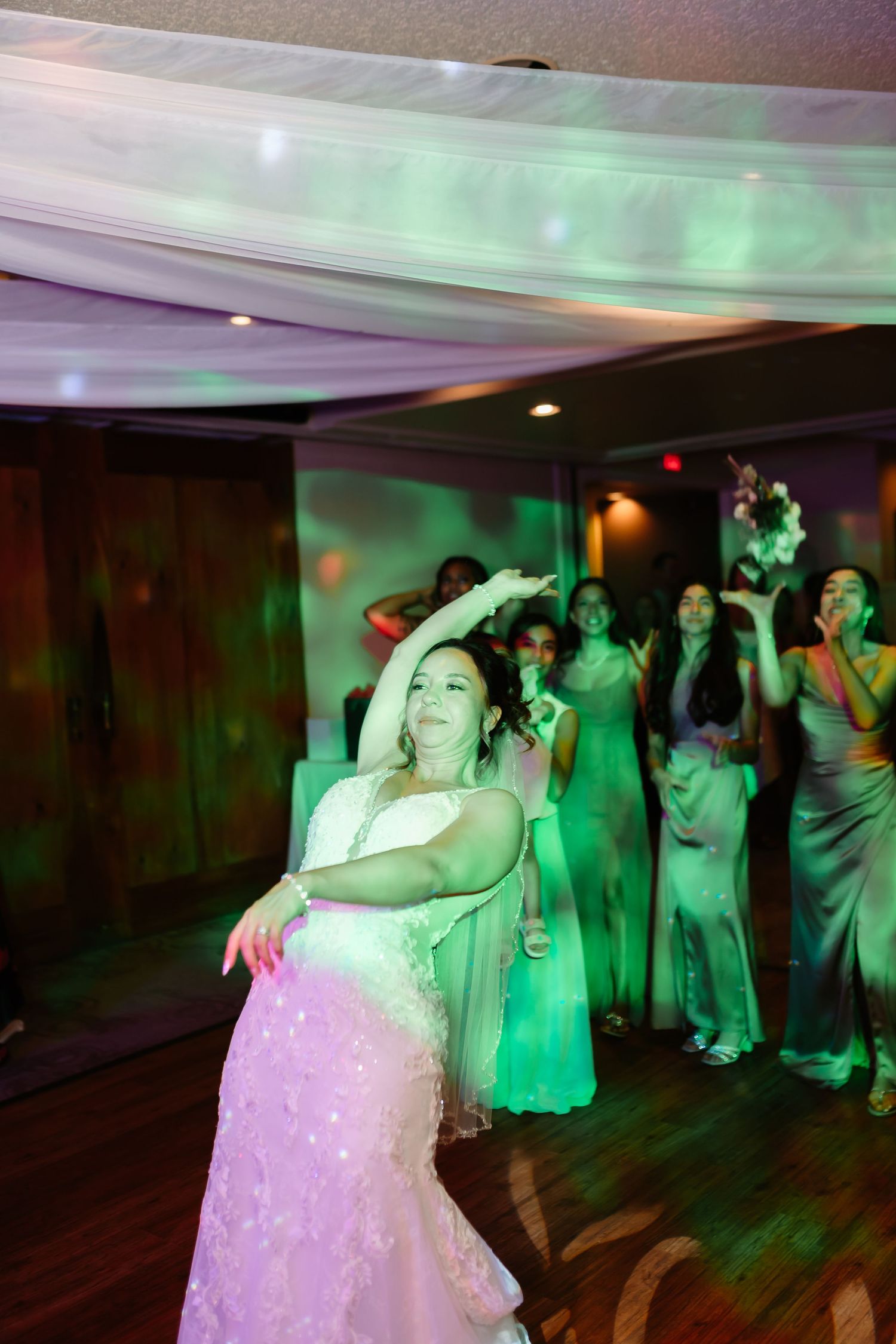 Wedding reception dance floor illuminated with colorful pink and green lighting.