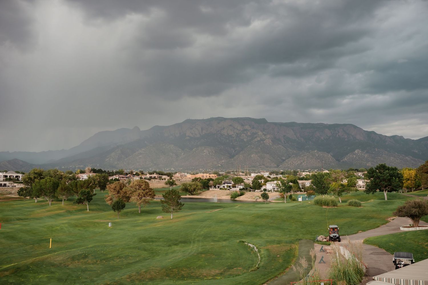 Scenic mountain landscape with green golf course and residential buildings under dramatic cloudy skies.