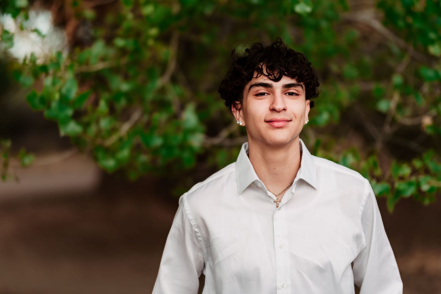 A young person in a crisp white button-down shirt smiles warmly against a soft, green leafy background.
