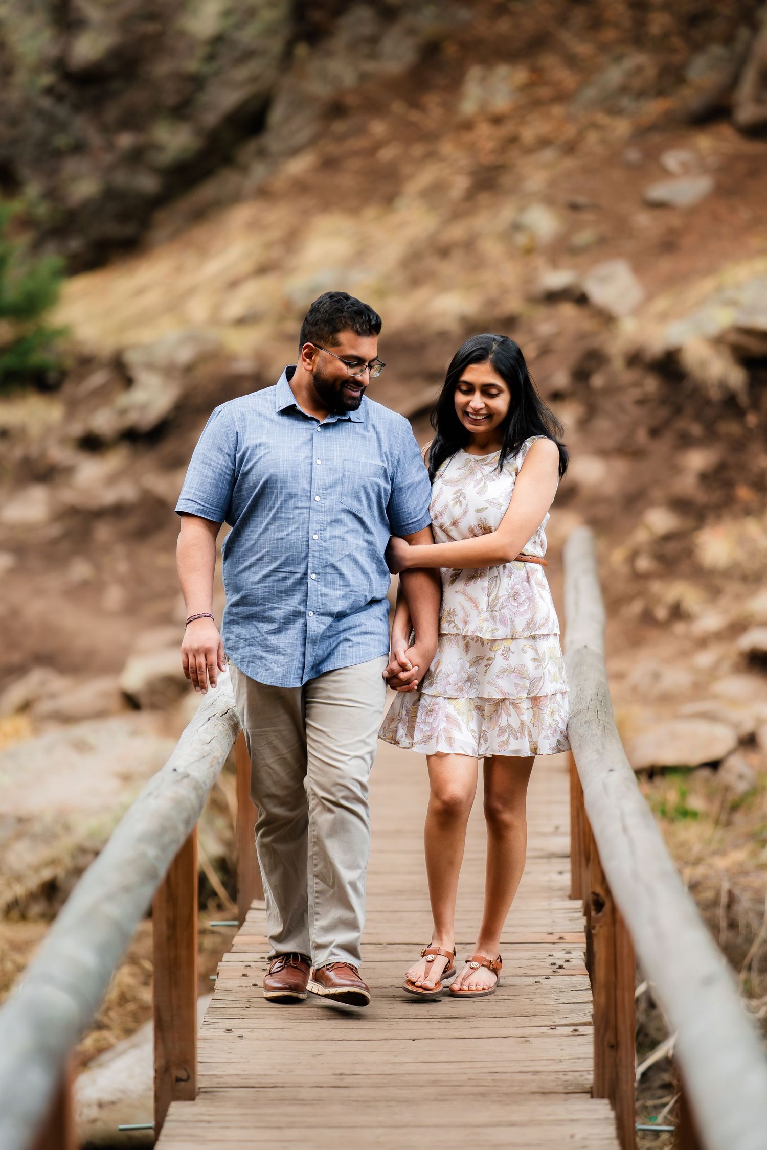 Couple walking hand in hand on a wooden bridge during their engagement photo session.