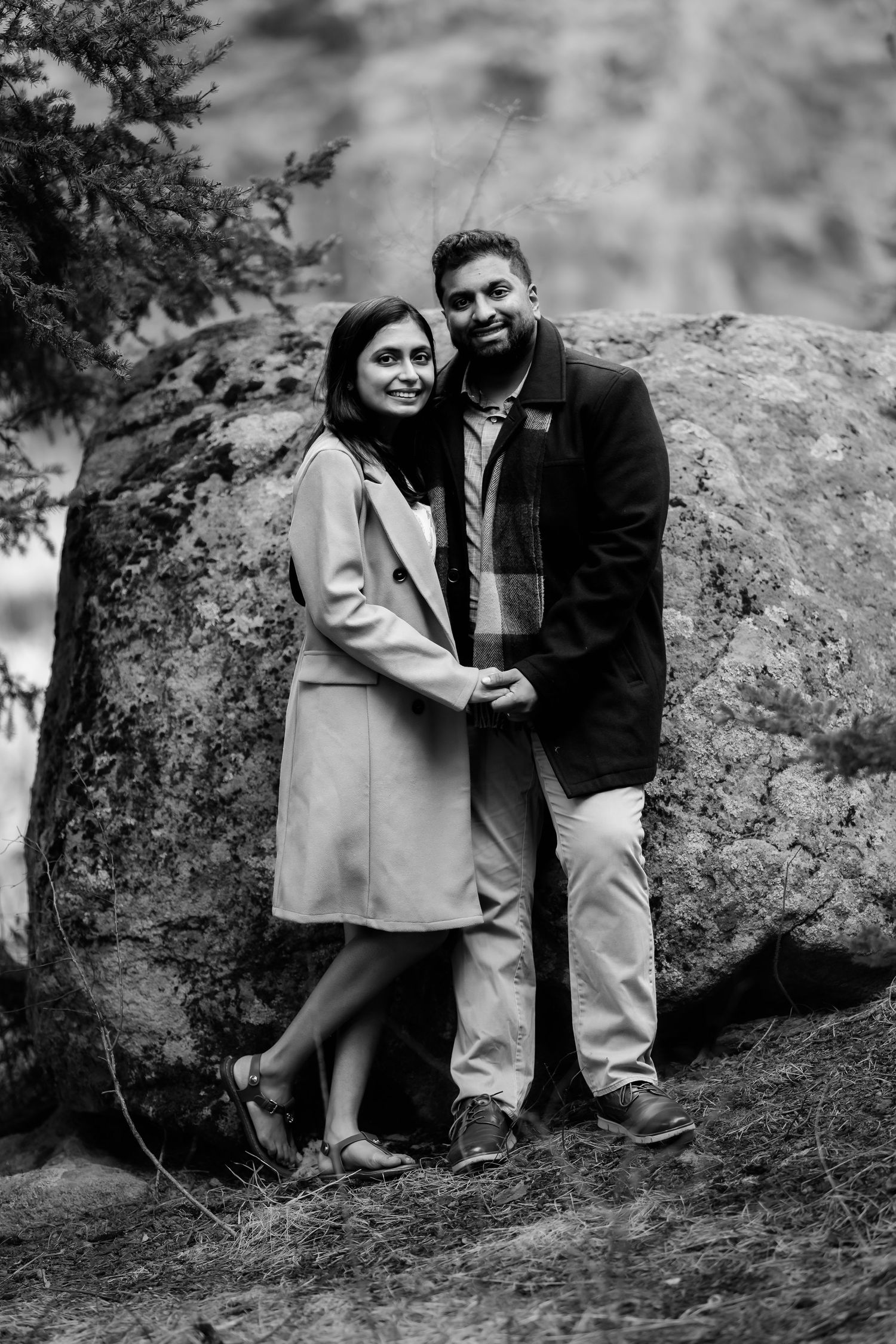 A black and white portrait of a couple standing against a large boulder.