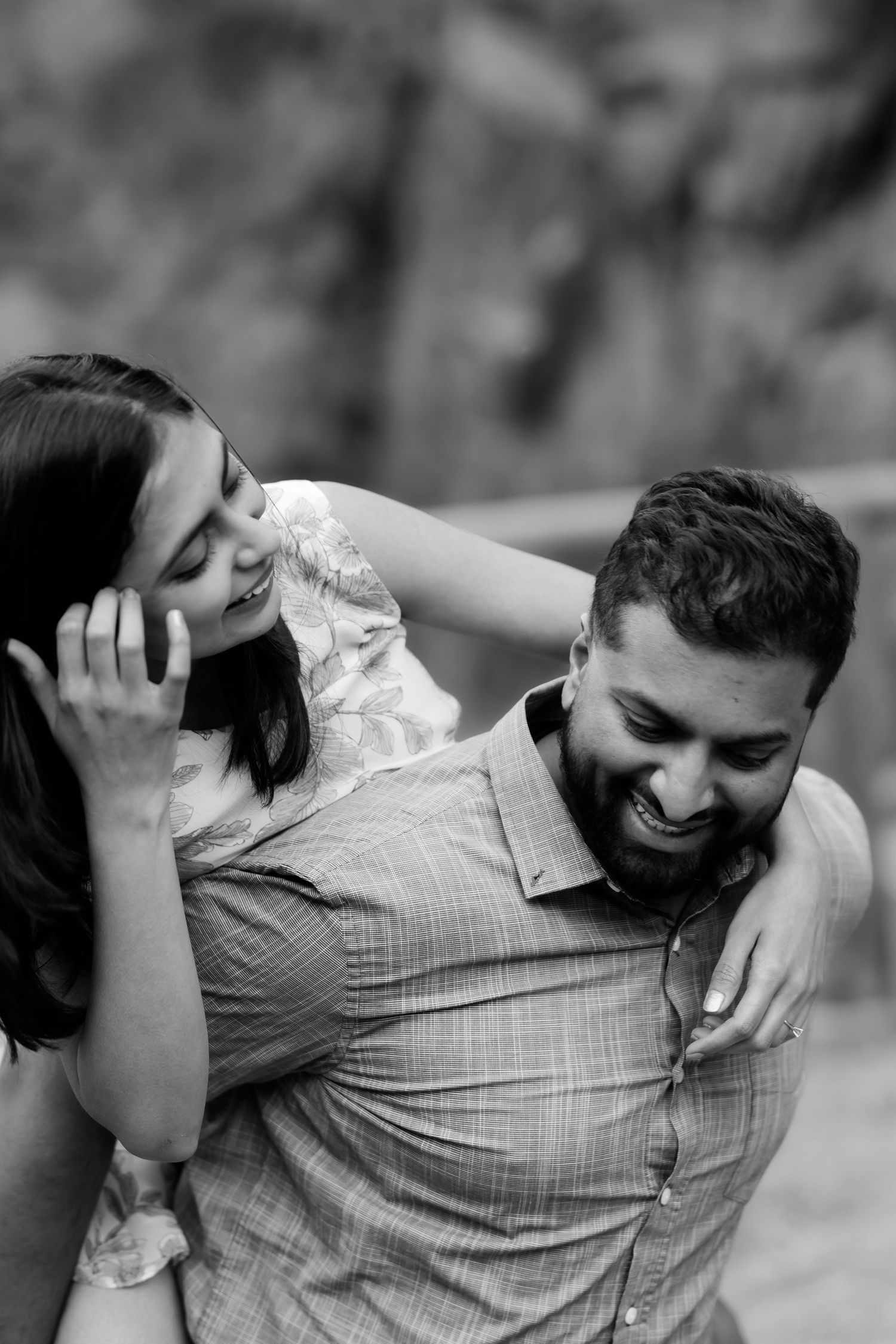 A couple shares a playful moment outdoors as they laugh together in black and white photography.