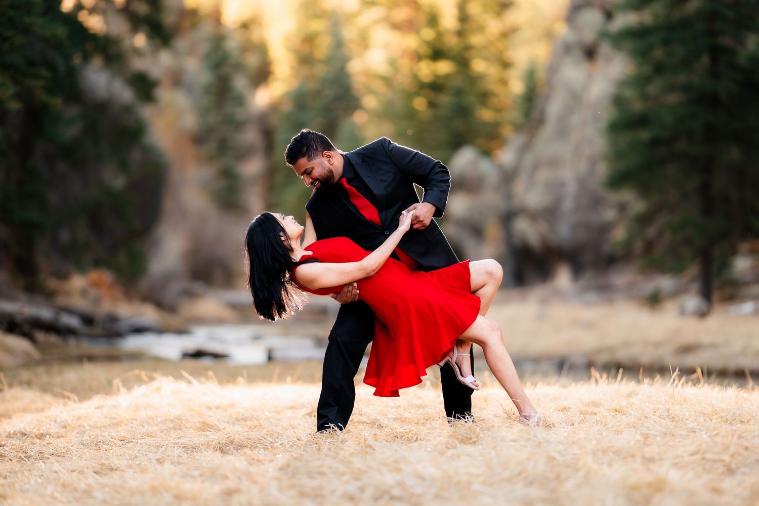 A romantic dance dip against a backdrop of evergreen trees and golden sunlight in a mountain setting.