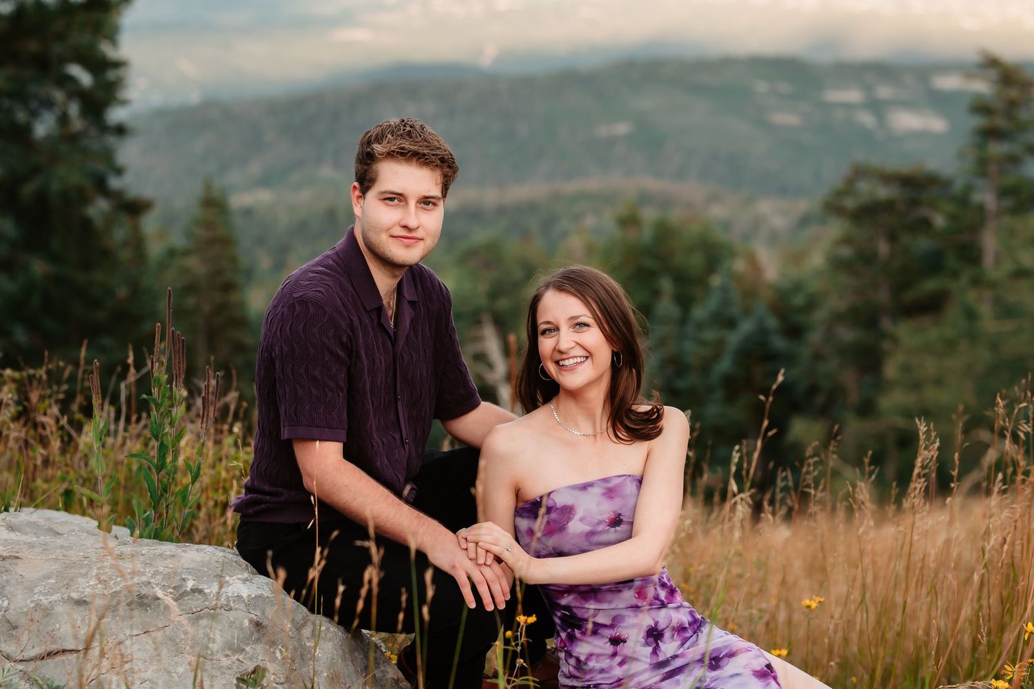 An engagement portrait on a mountain with a purple dress and casual attire.