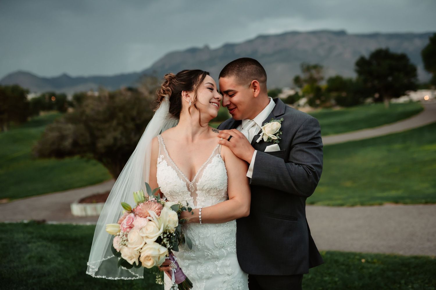 A couple embraces on a grassy hill during a wedding photoshoot with mountains in the distance.