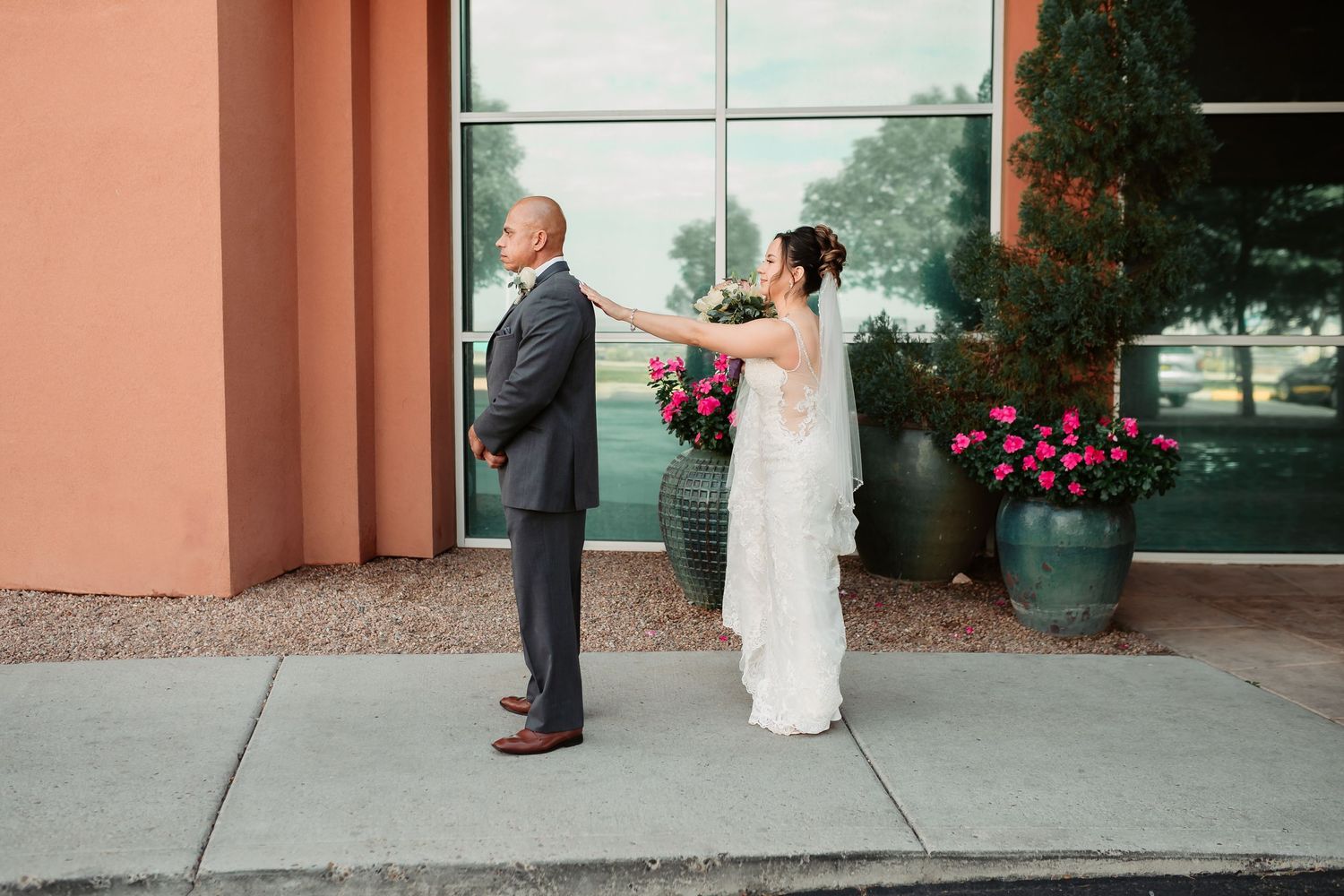 A couple seen from a distance share a loving moment during their wedding ceremony outside a building entrance.