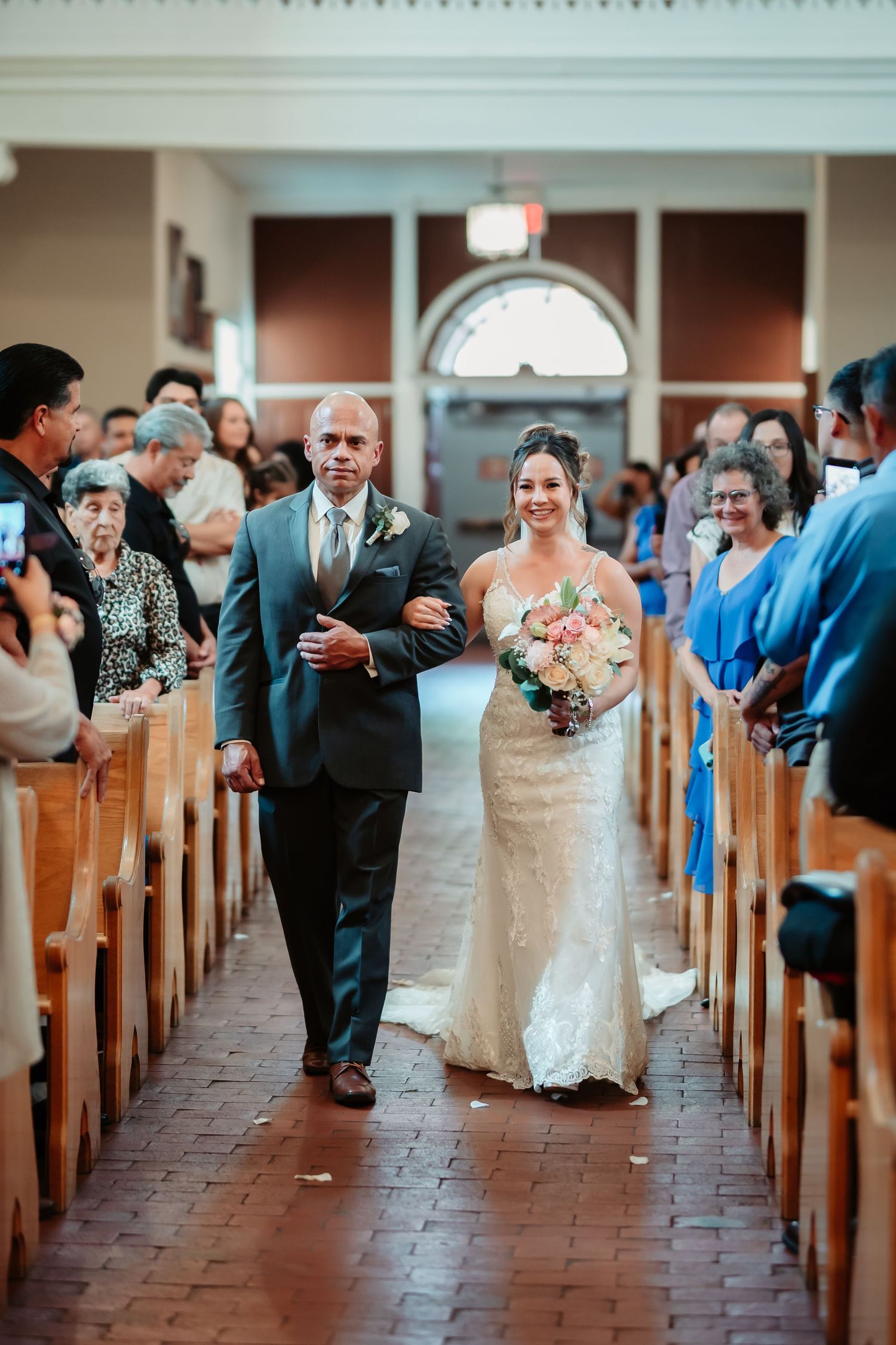 Wedding procession walking down church aisle with guests in blue attire looking on.