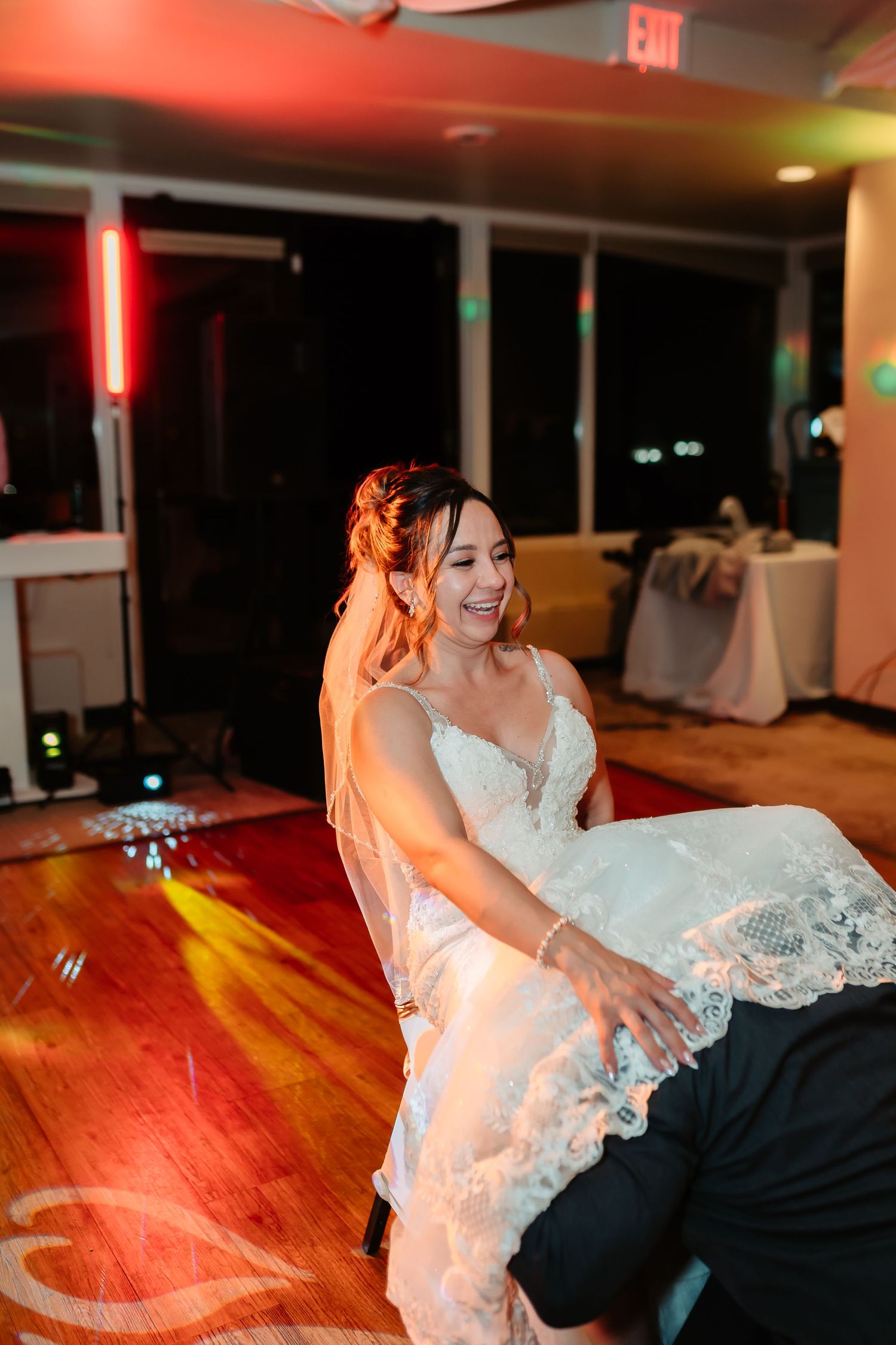 A couple shares a playful dance moment on a polished hardwood floor illuminated by red ambient lighting.