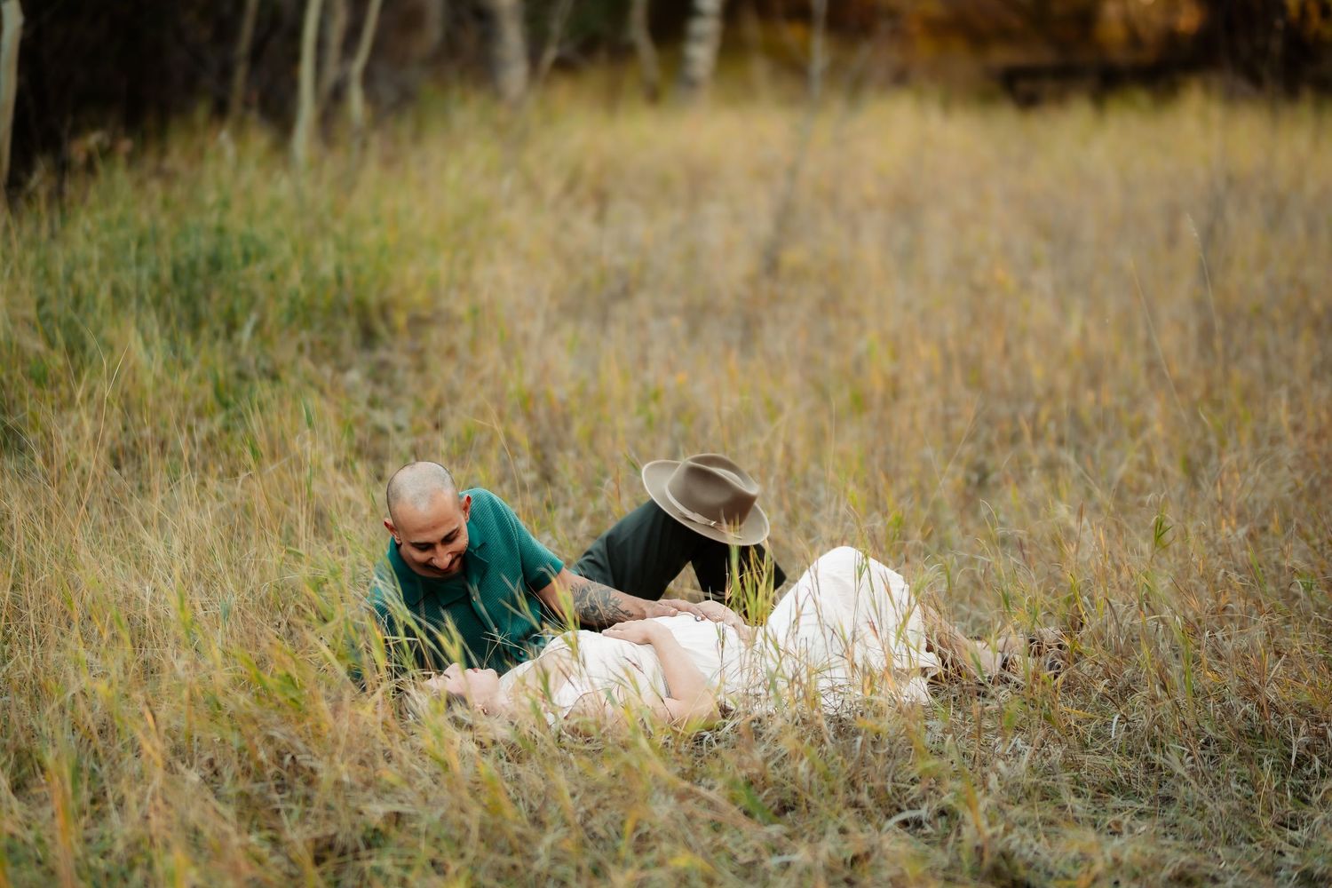 A couple walks hand in hand through a golden autumn meadow with tall grass and sunlit scenery.