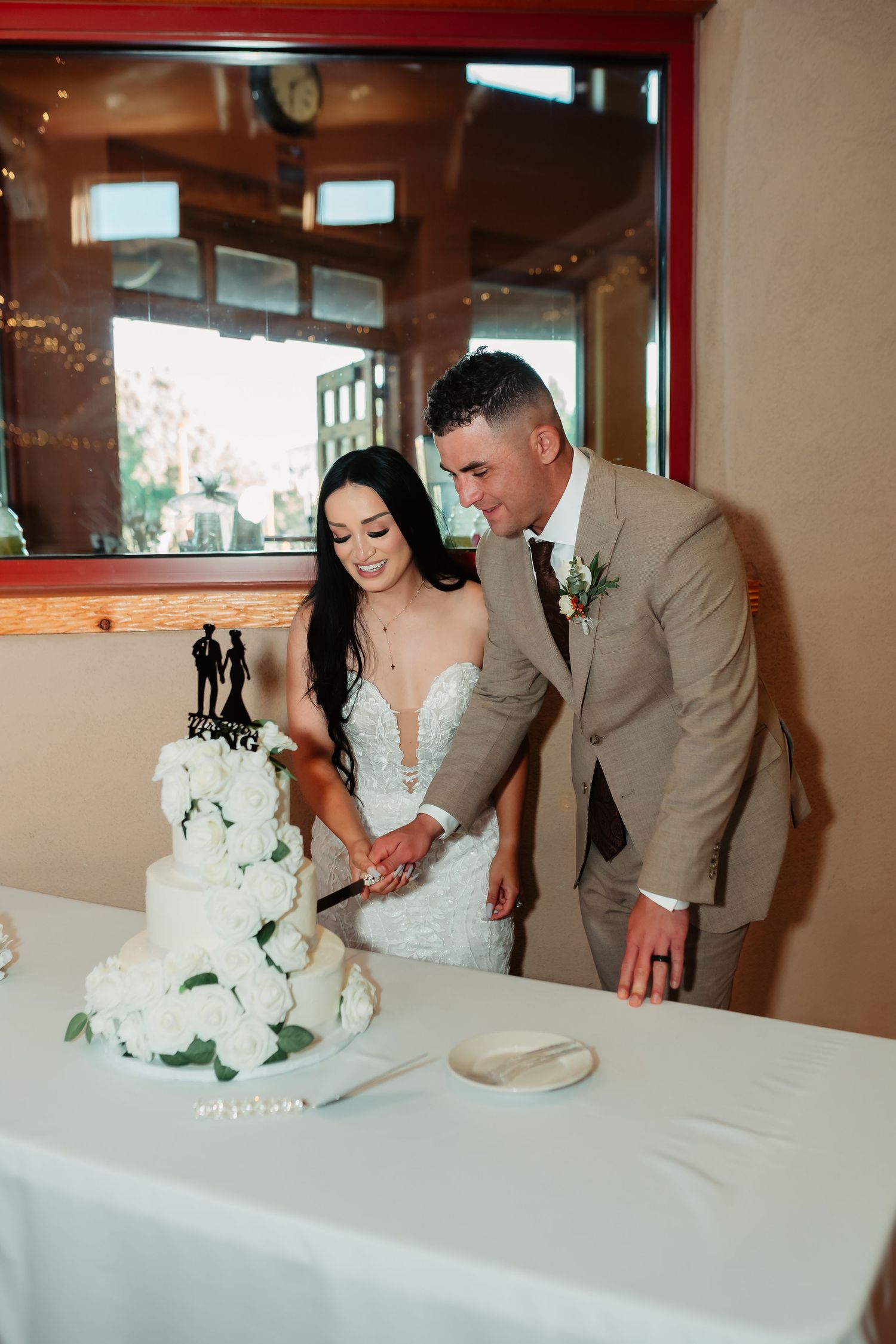 A couple in wedding attire cuts their elegant white tiered wedding cake together at their reception.