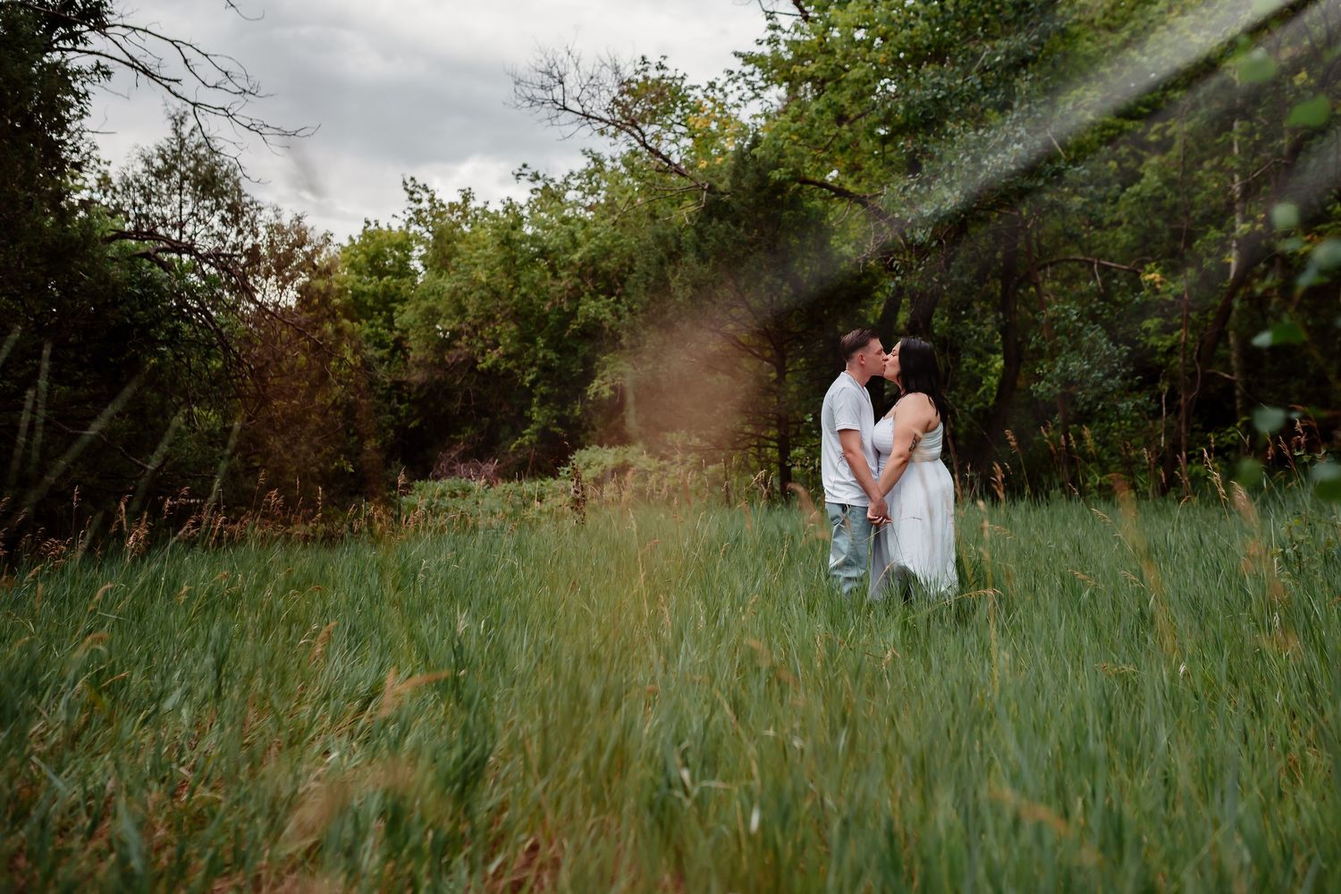 Couple stands in a lush green meadow under moody skies during an intimate outdoor photo session.
