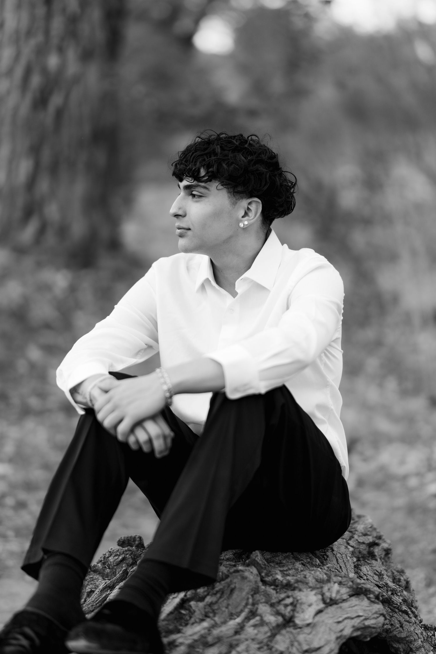 Black and white portrait of someone in white shirt sitting on a rock in a natural setting.