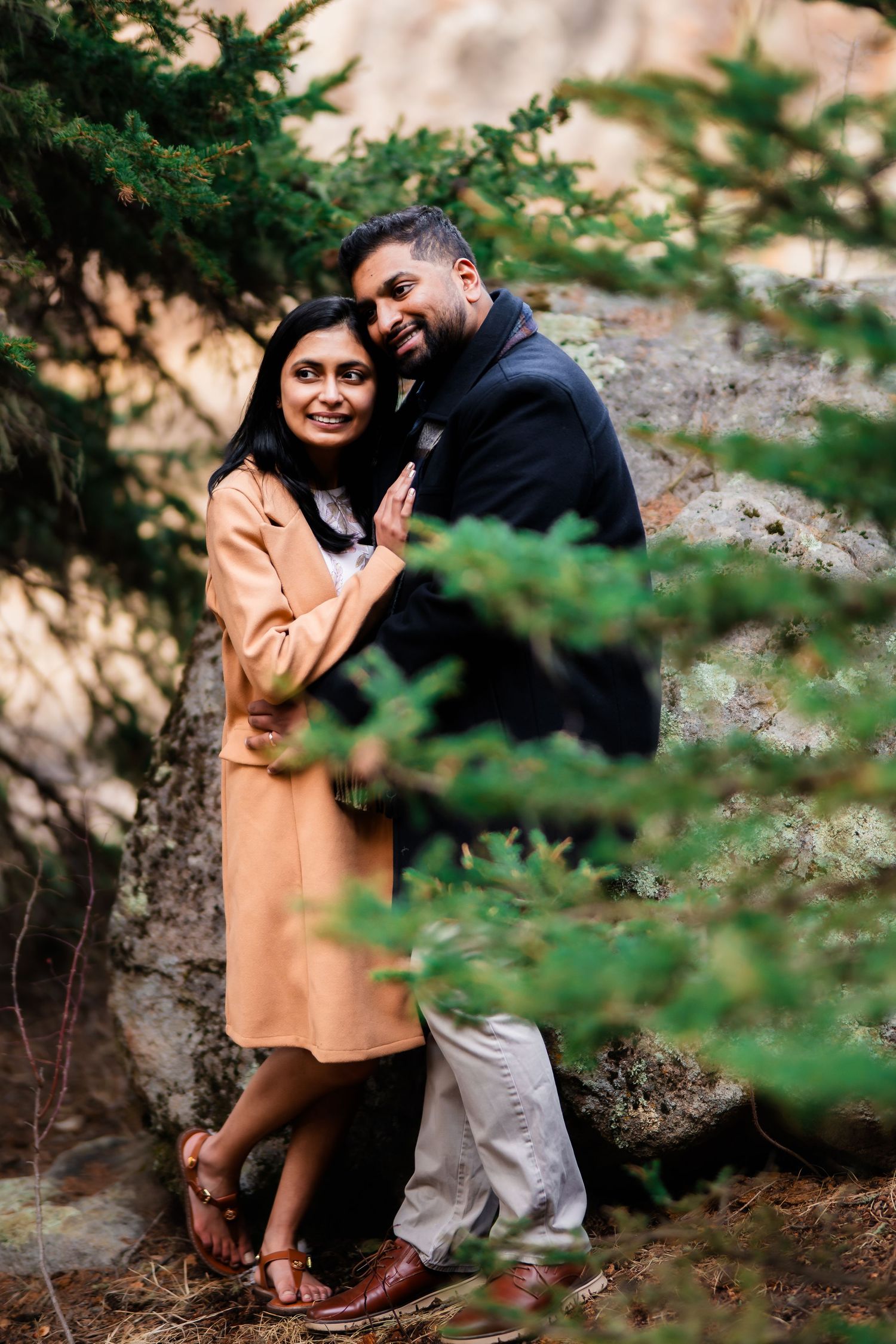 Loving couple shares intimate moment against rocky backdrop while dressed in autumn attire.