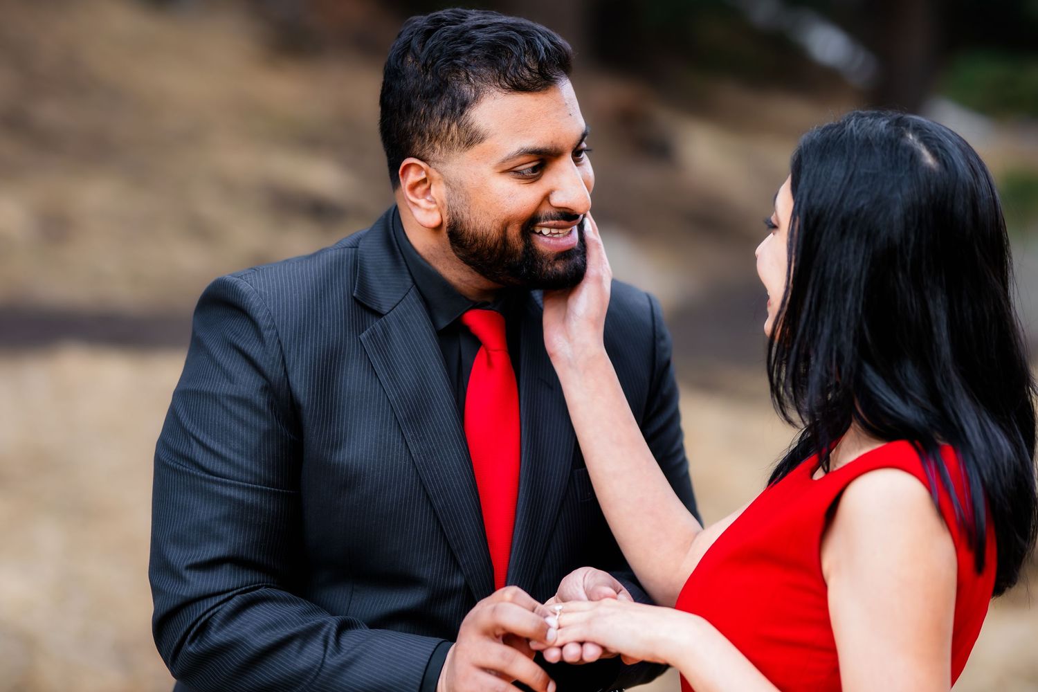A tender moment between a couple in formal wear against a natural outdoor backdrop.