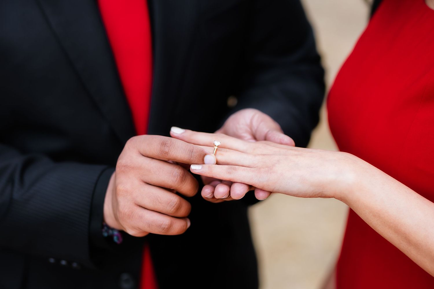 Close-up of hands exchanging a ring during an engagement, with formal attire visible.