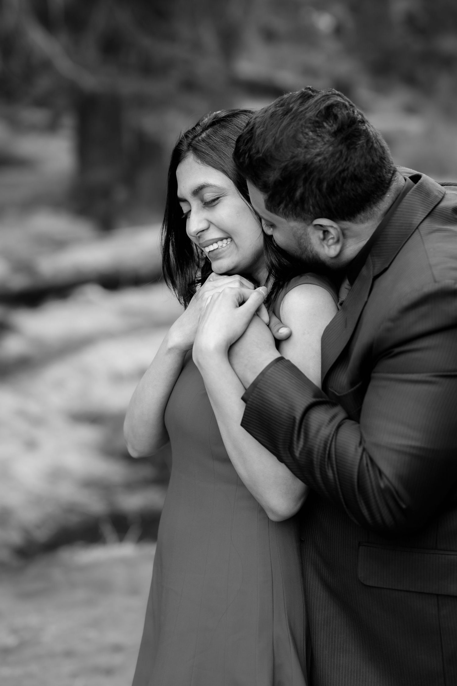 An intimate black and white portrait of an embracing couple sharing a tender moment outdoors.