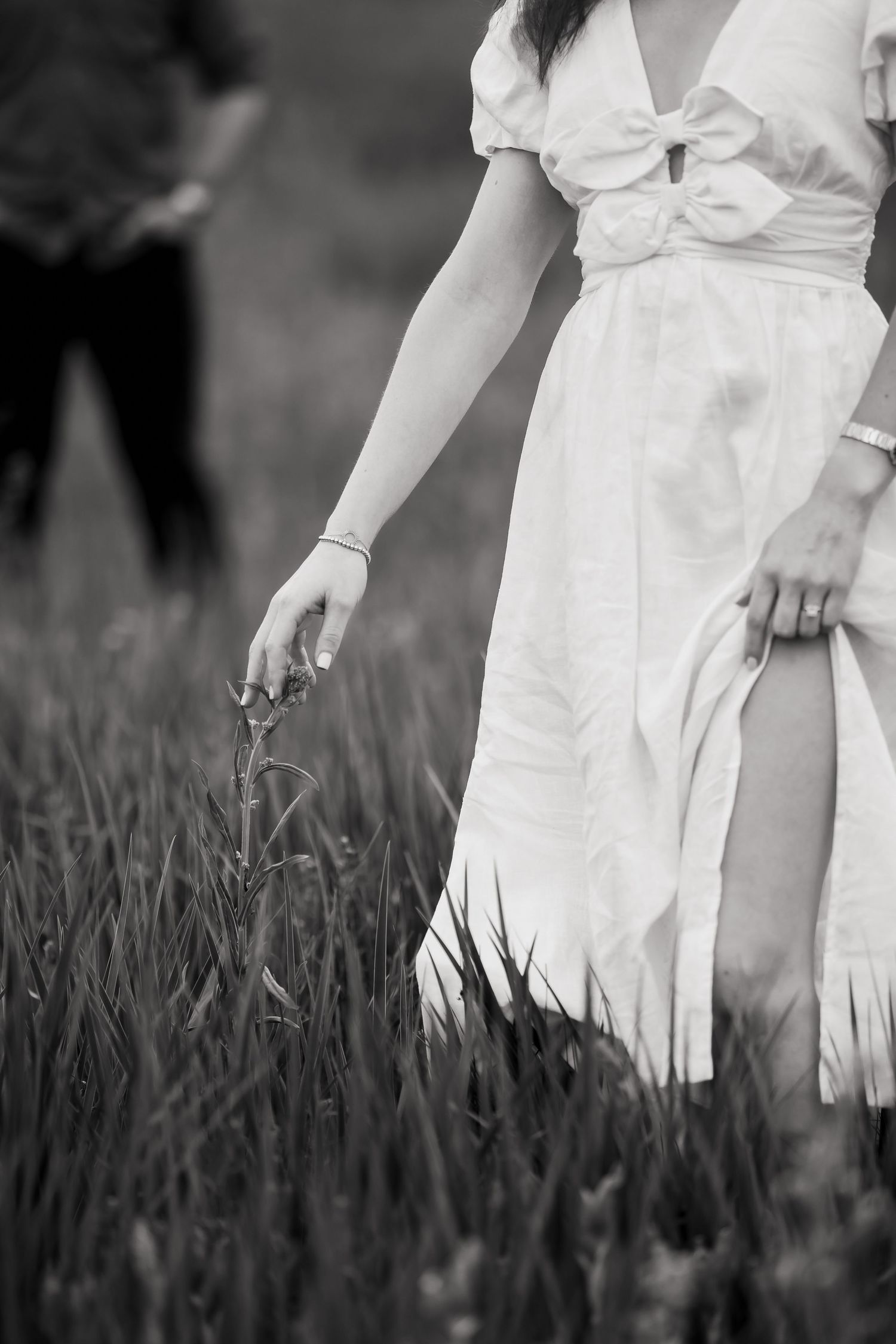 A person in a flowing white dress walks through tall grass in a black and white photograph.