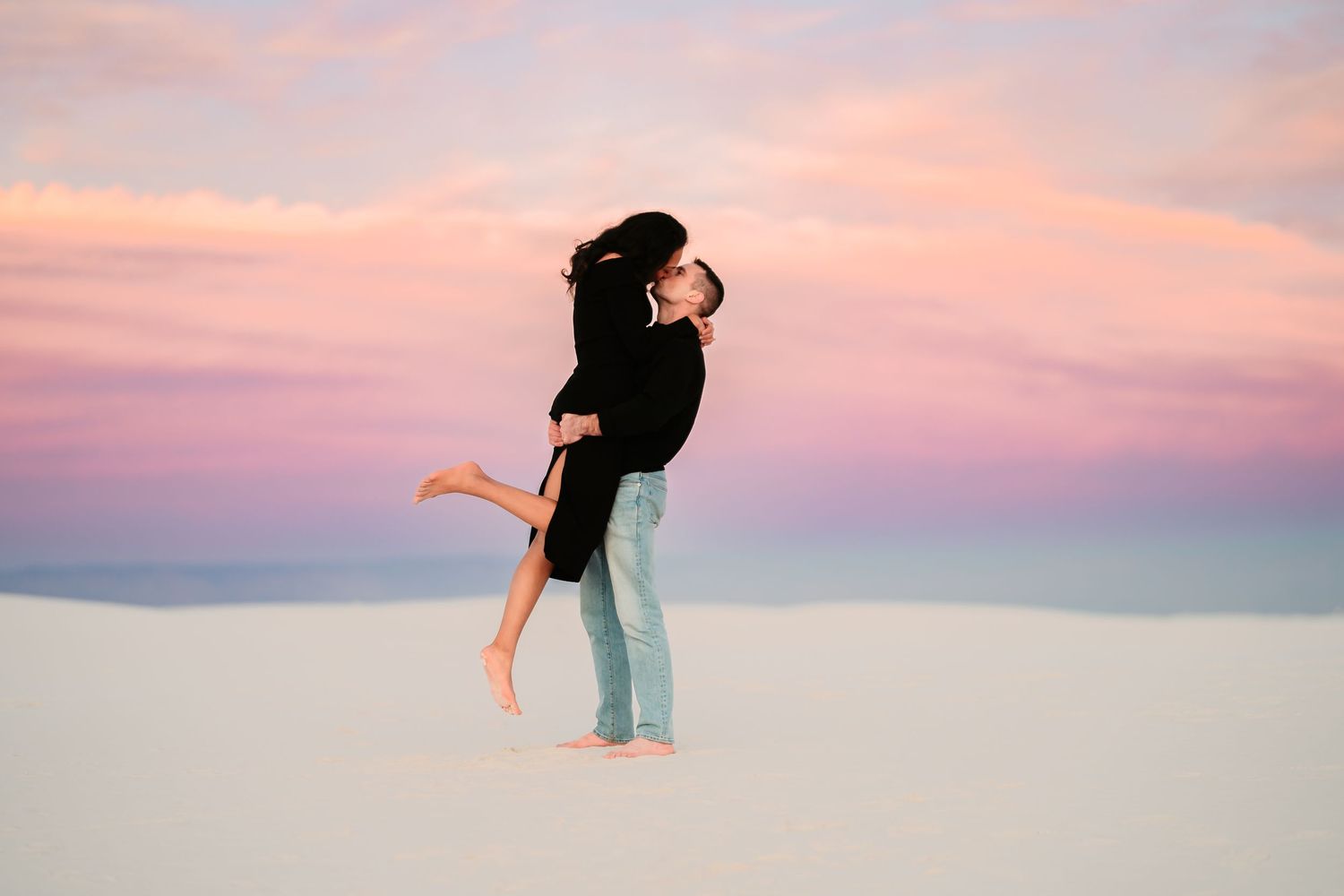 Silhouetted figures dance and pose against a dreamy pink and purple sunset sky at the beach.