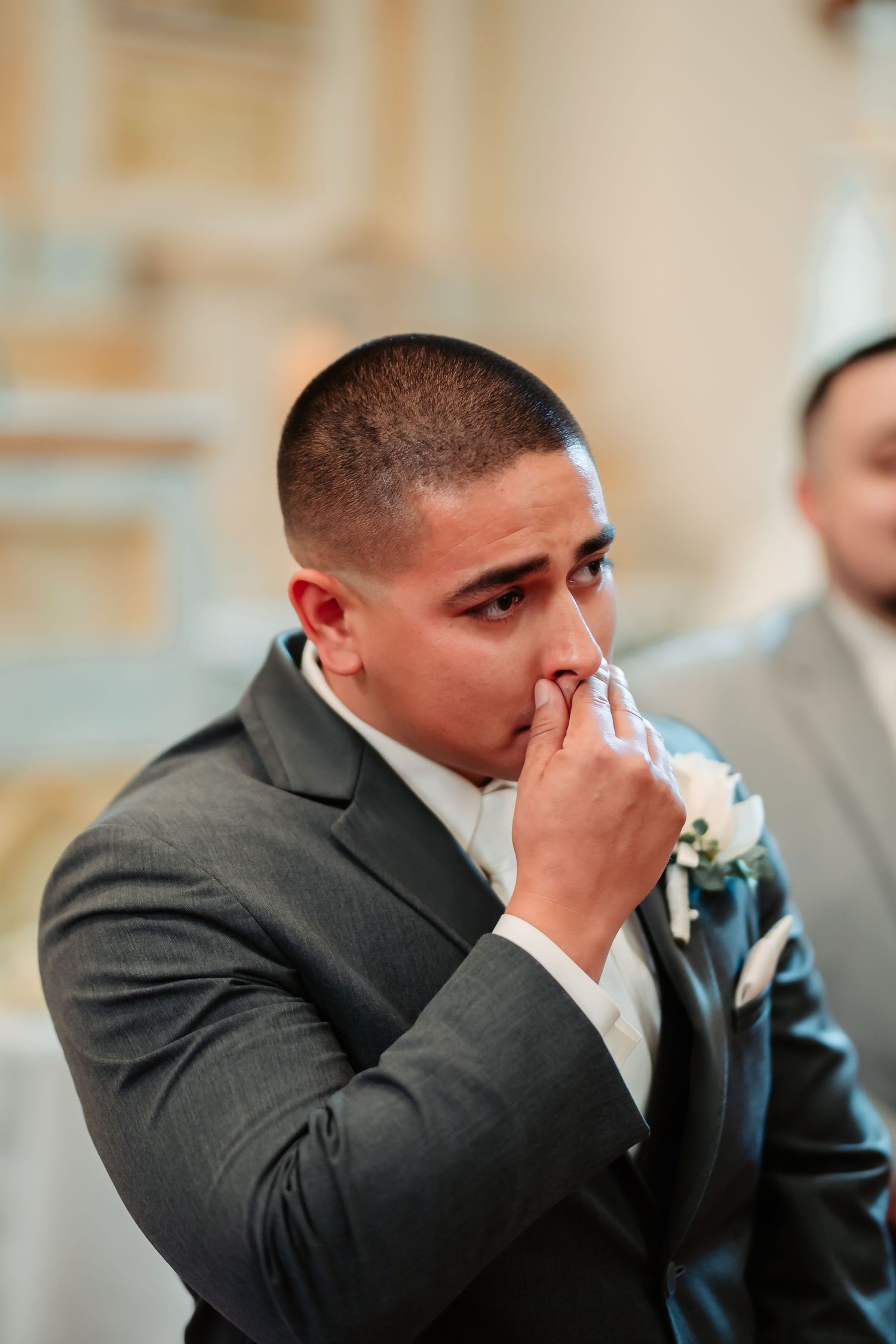 Emotional moment captured as a man in a grey suit wipes tears during a wedding ceremony.