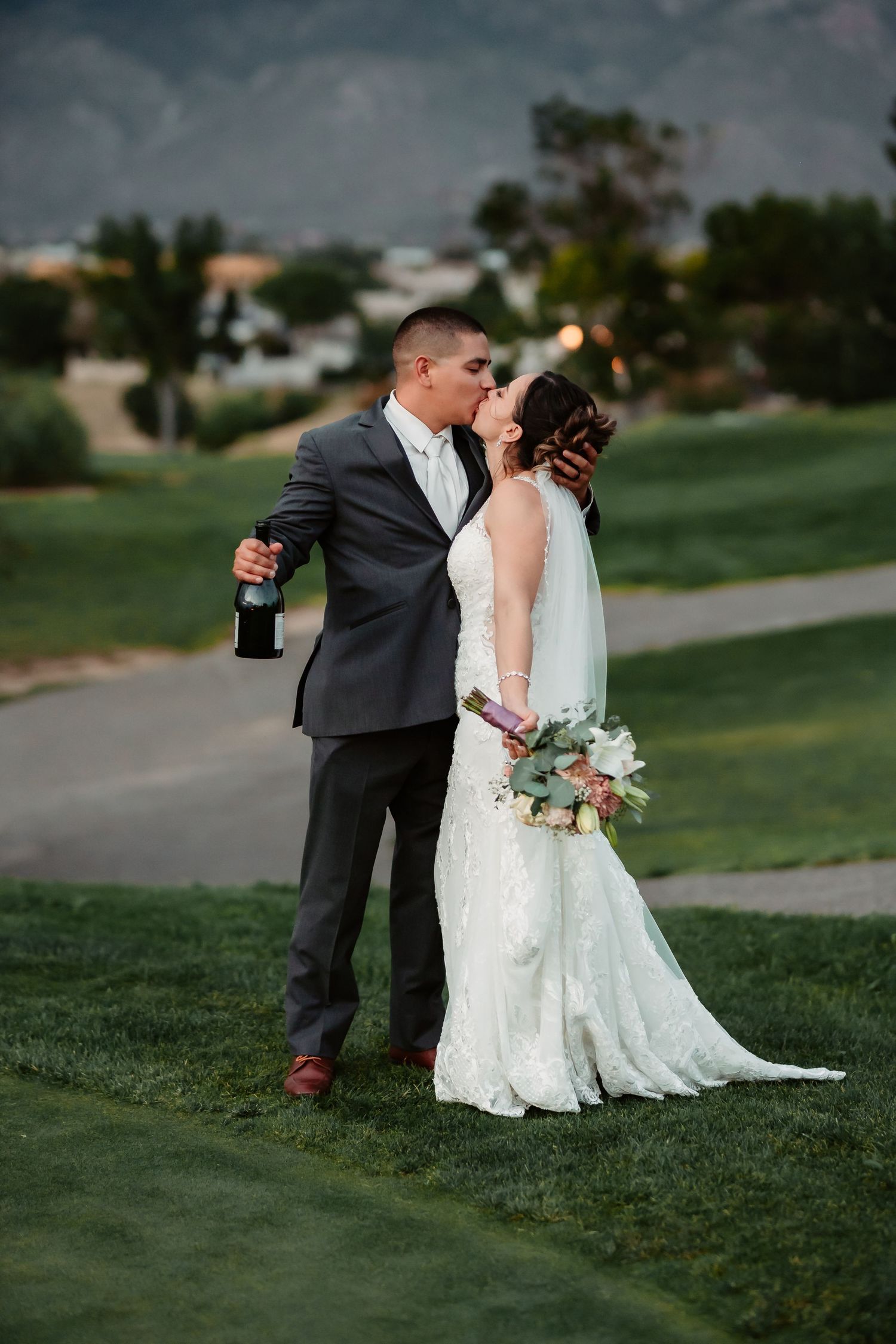 Wedding couple poses playfully on golf course with mountain scenery.