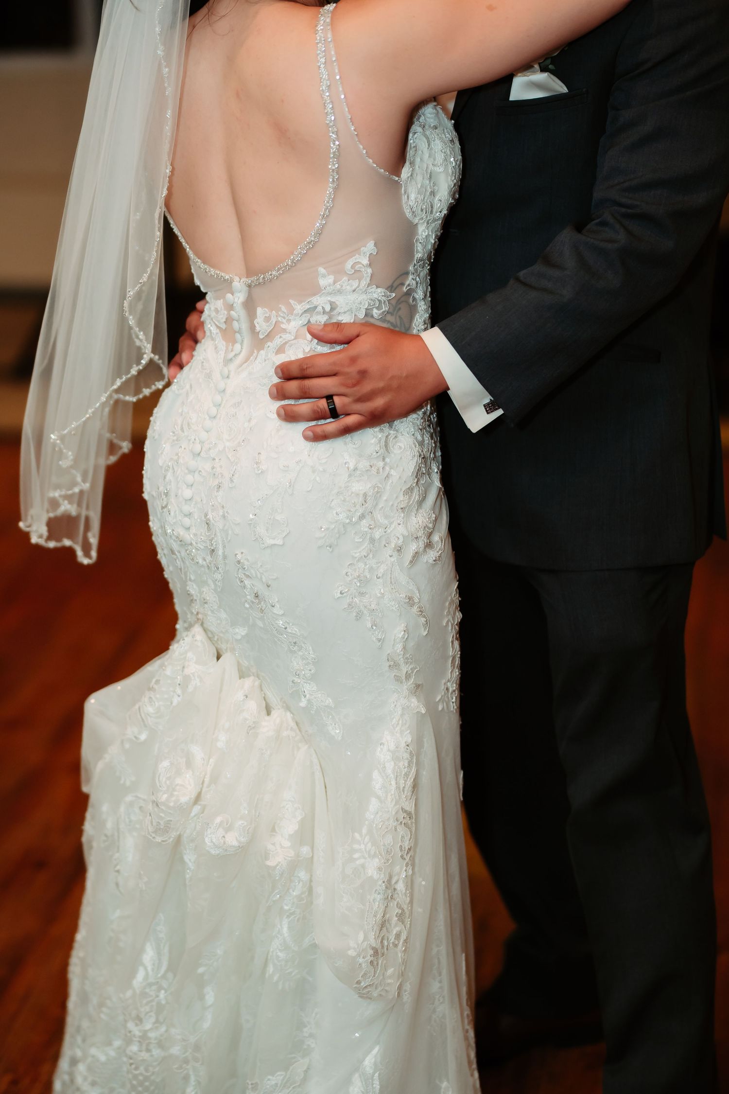 Close-up details of intricate lace and beading on a white wedding dress with sheer back panels.
