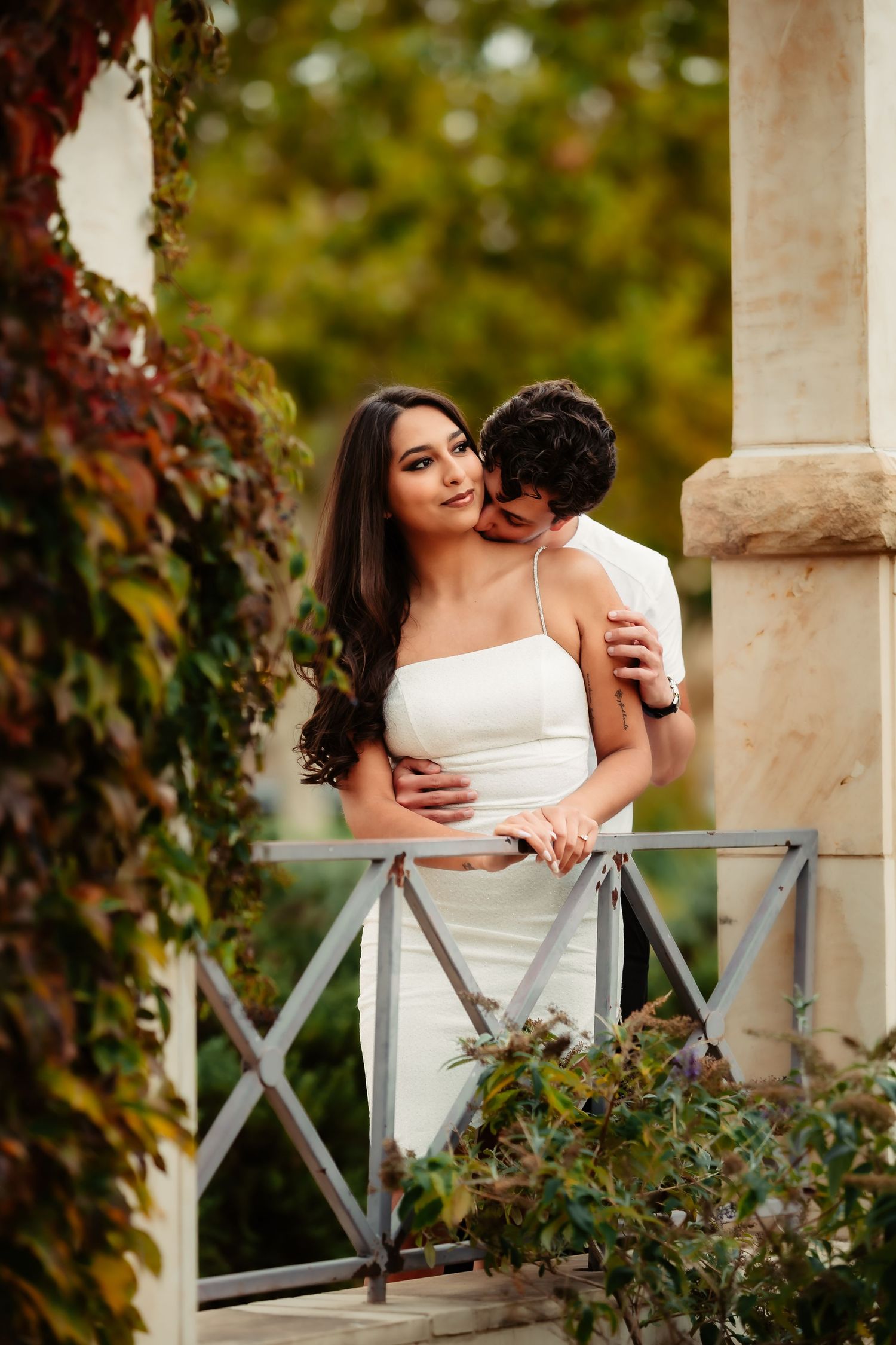 A romantic moment shared between a couple on a porch with autumn foliage in the background.