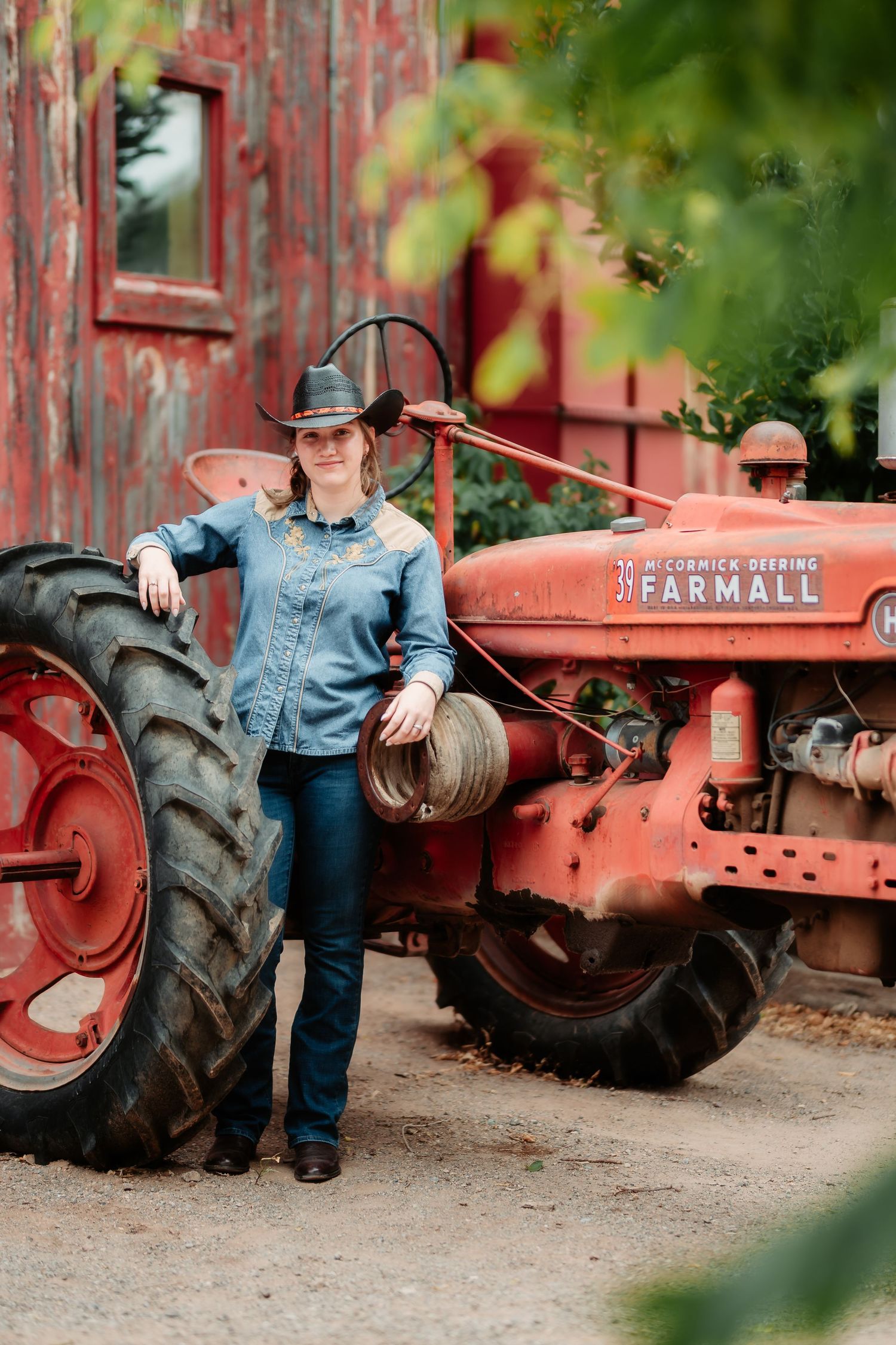 A vintage red Farmall tractor serves as a rustic backdrop for a country-style portrait session in denim attire.