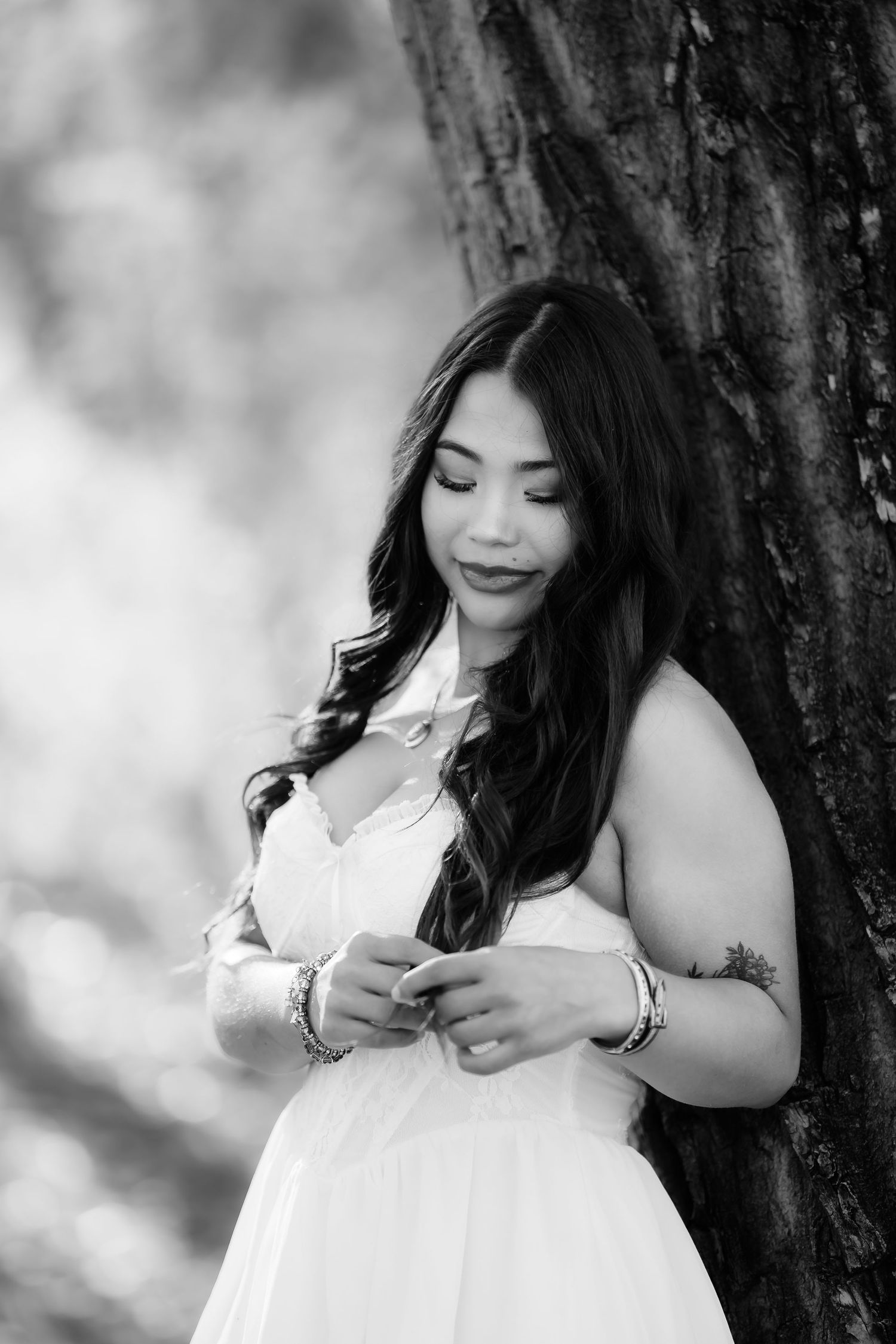 Black and white portrait series showing woman in white dress posing against tree trunk.