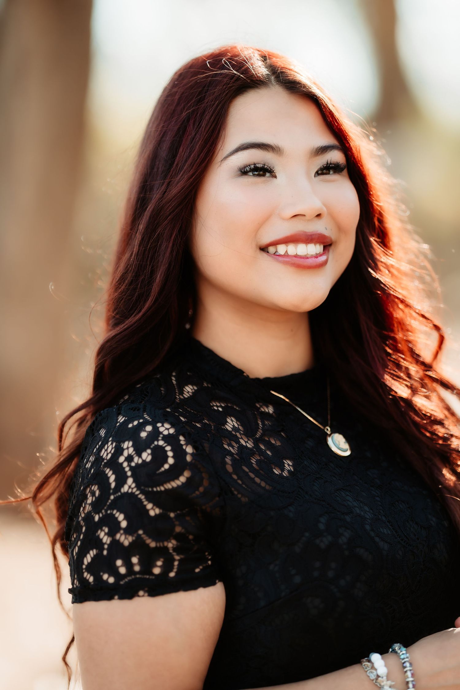 Professional portrait in black lace top with warm lighting and natural makeup against blurred background.