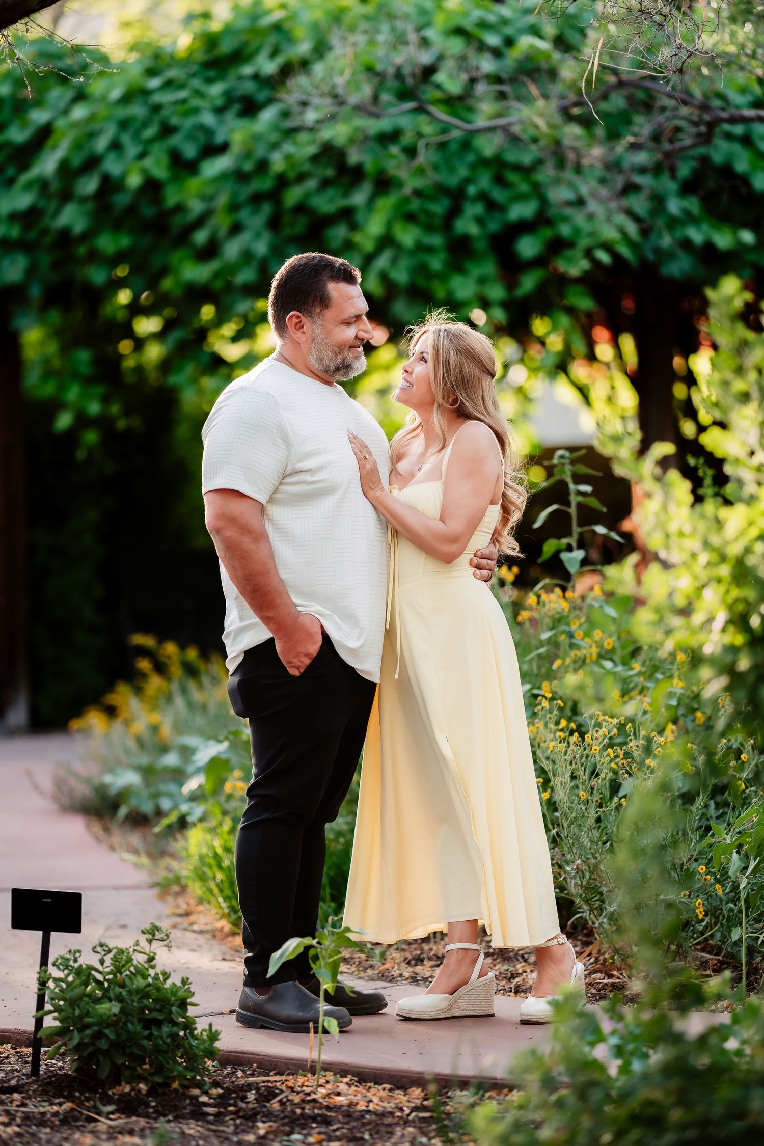 A couple shares a romantic moment in a lush garden setting with golden sunlight filtering through the trees.