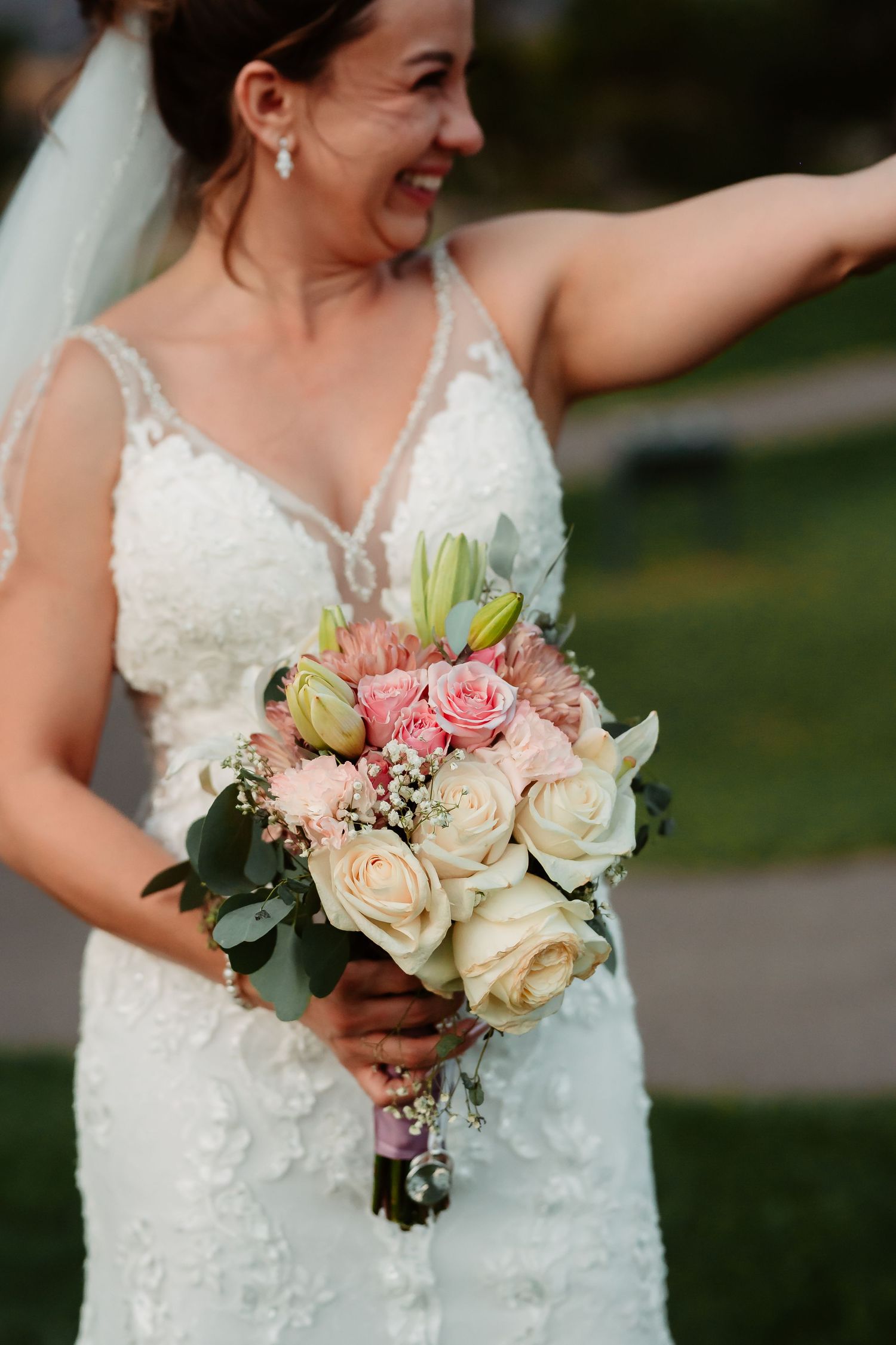 Wedding bouquet with soft pink and cream roses held against a white lace gown.