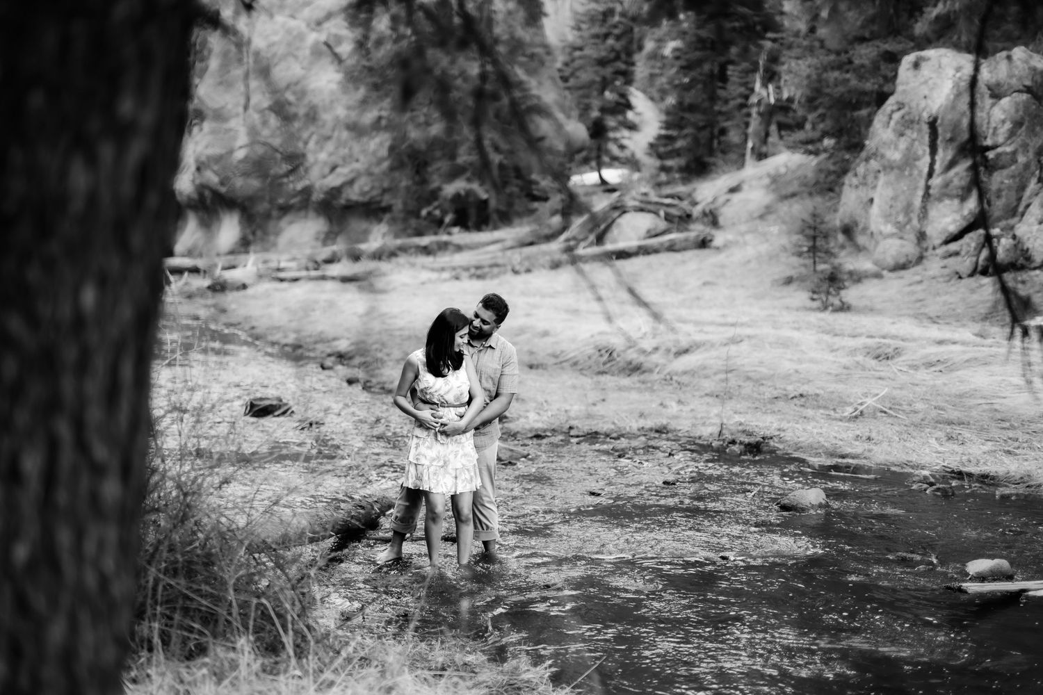 A black and white photograph of a couple embracing by a mountain stream.